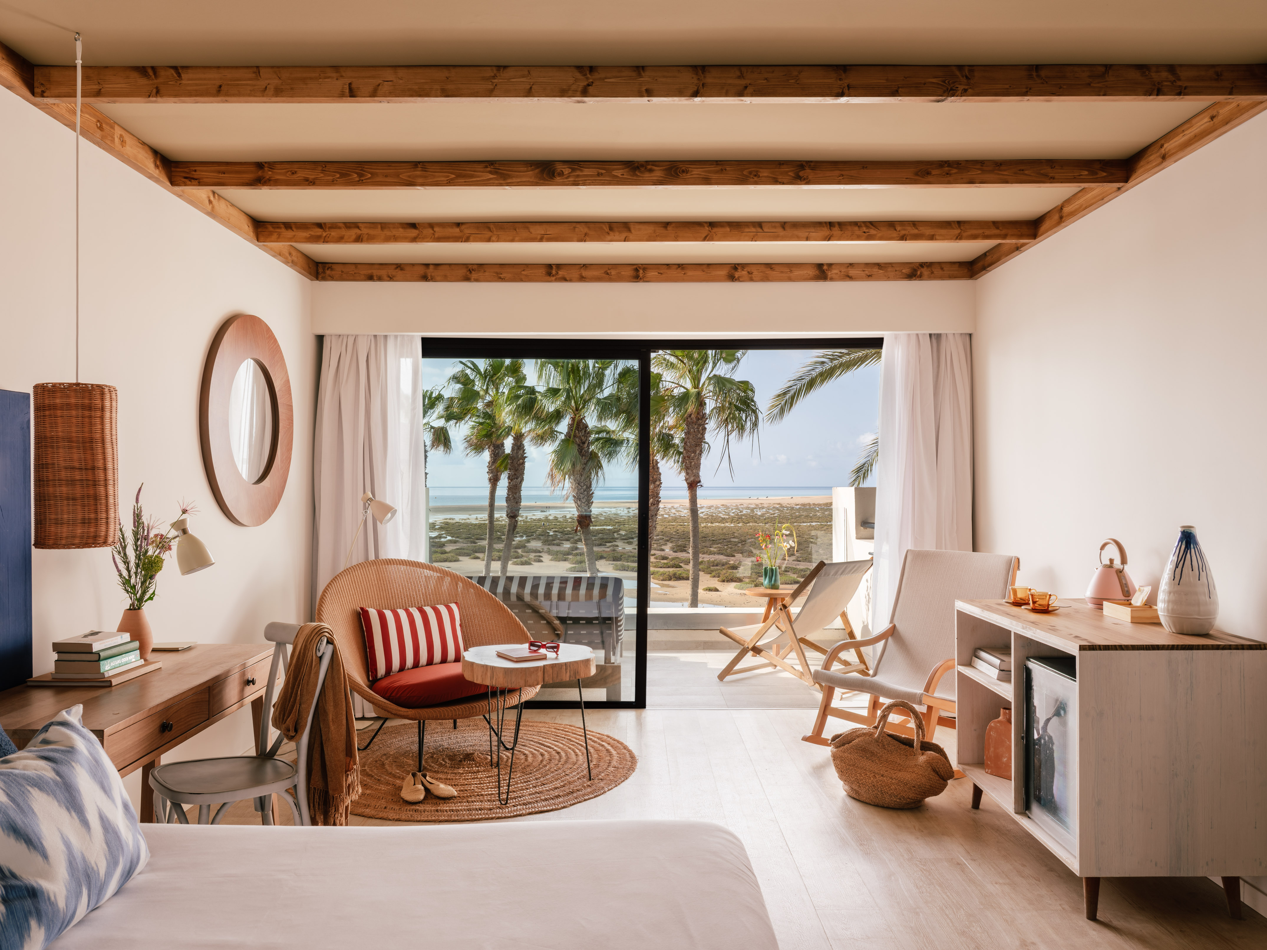 Habitación de hotel con vista al mar, palmeras y decoración costera clara.