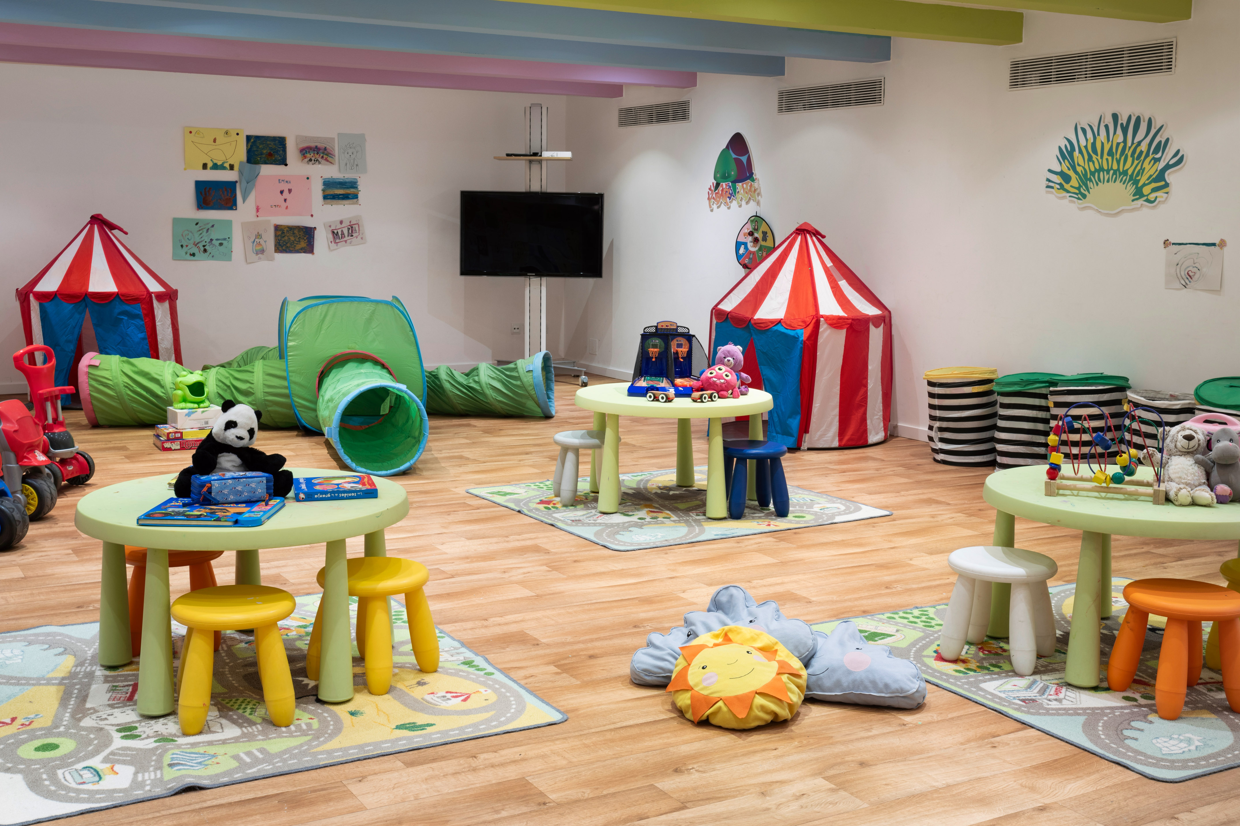Colorful kids' playroom with play tunnels, tents, small tables, chairs, and toys.