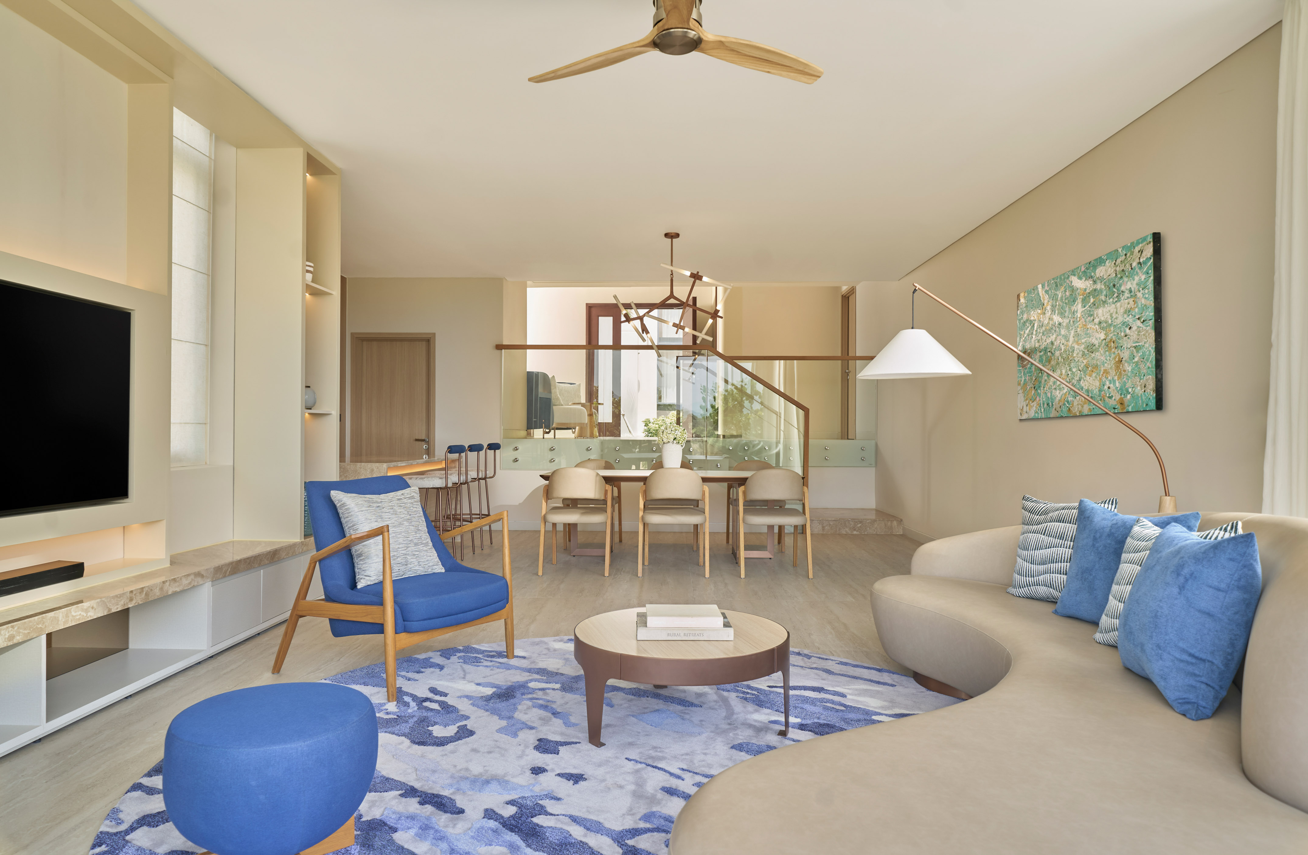 Modern living and dining room with blue accents, beige sofa, and wood details.