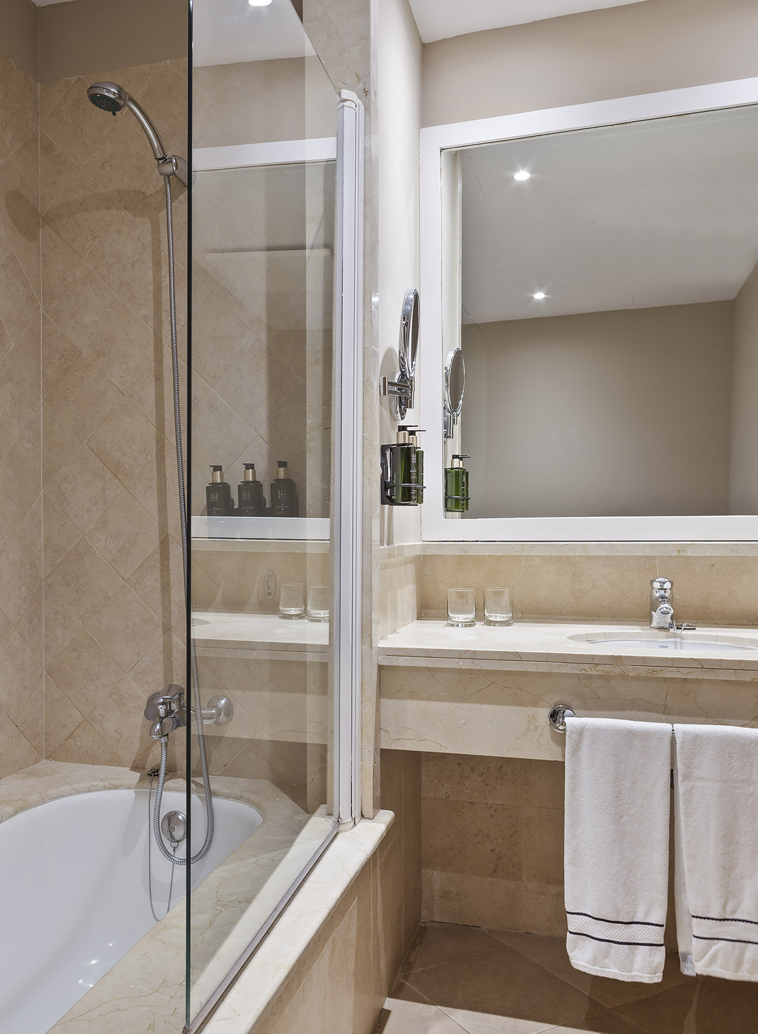Hotel bathroom with shower-bathtub, beige tiled walls, vanity, mirror, and towels.
