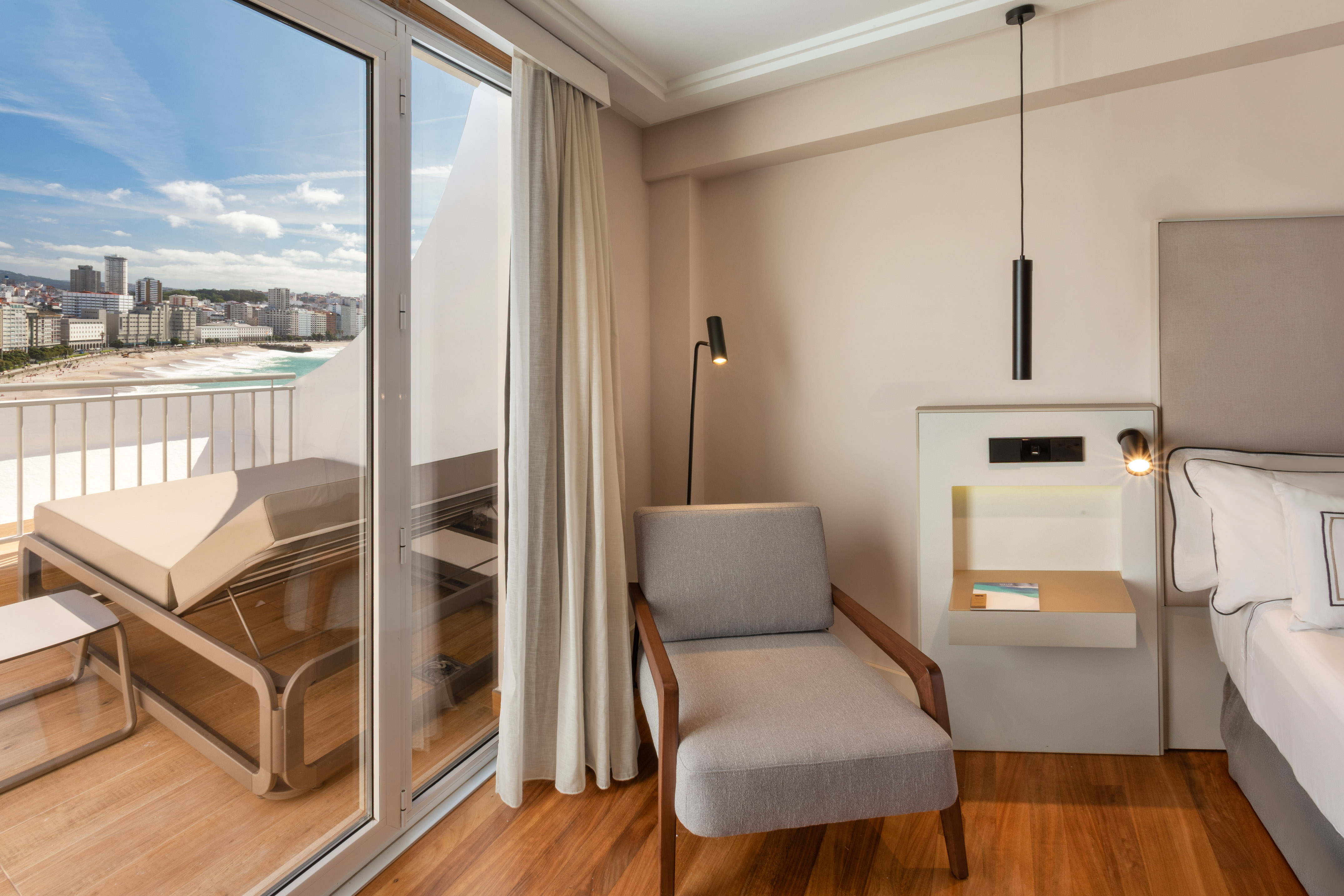 Modern hotel room with balcony, ocean view, beach, and city skyline.