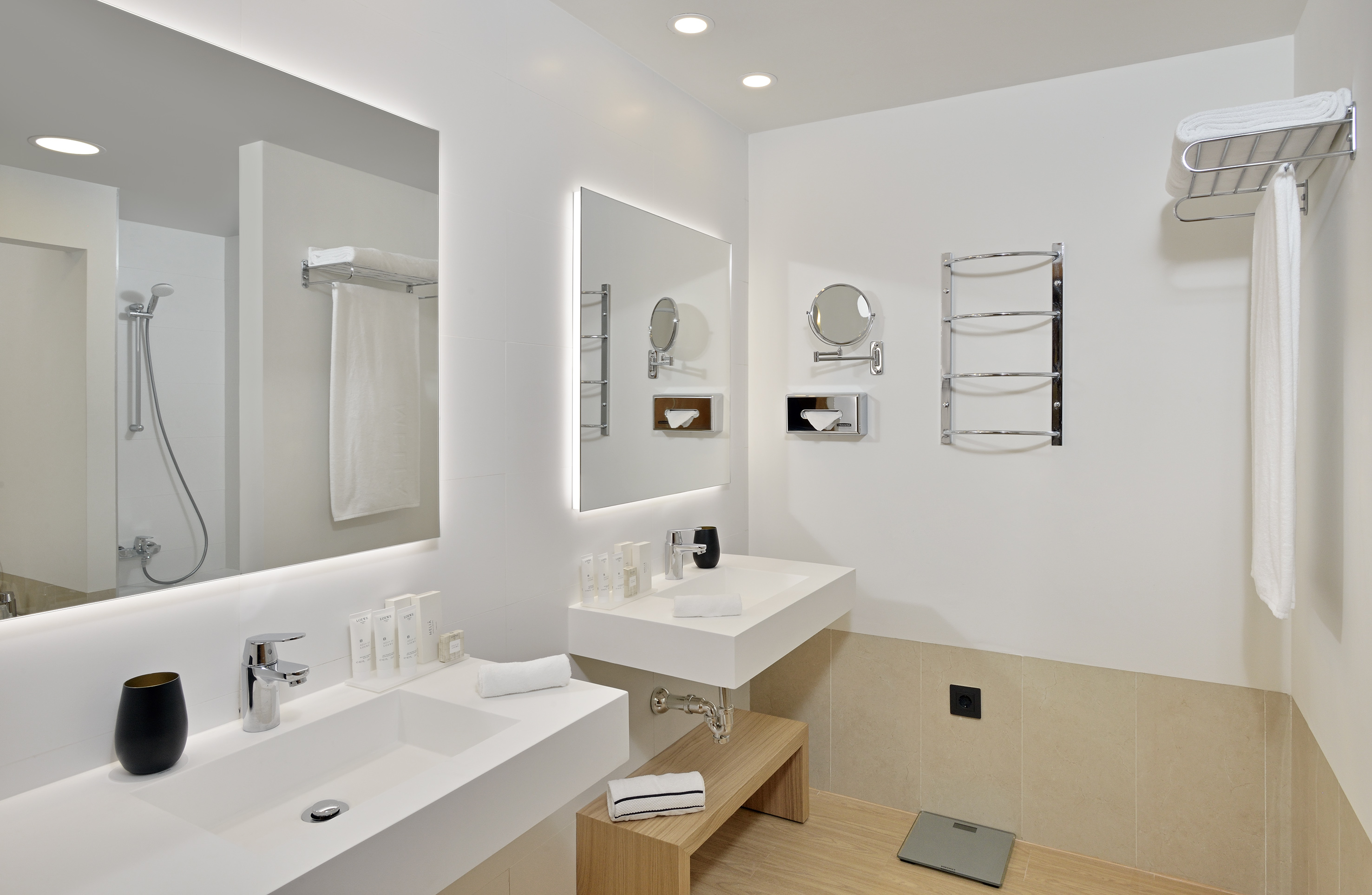 Modern hotel bathroom with double vanity, illuminated mirrors, and shower.