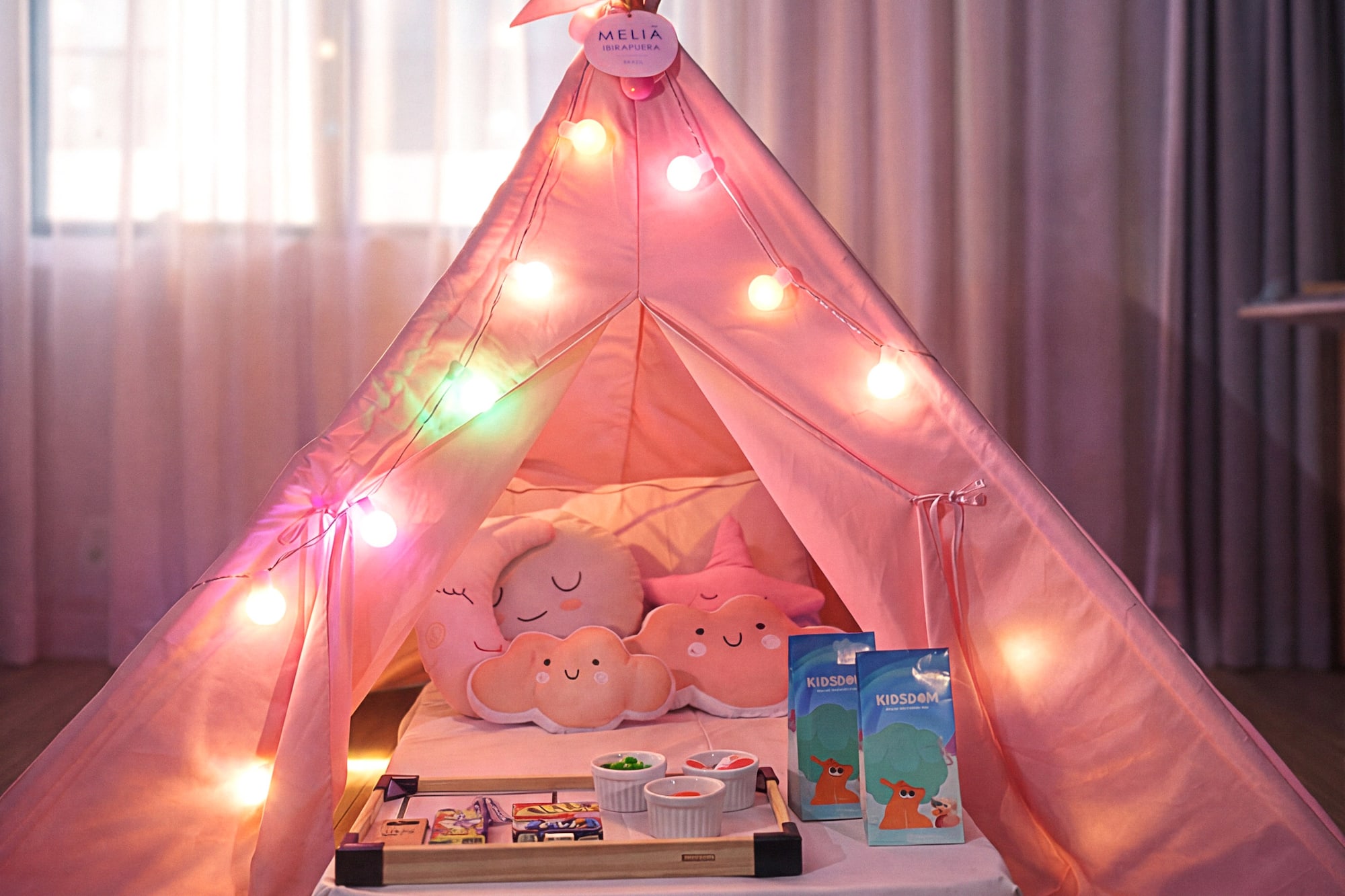 Pink Melia kids' play tent with string lights, pillows, and snack tray.