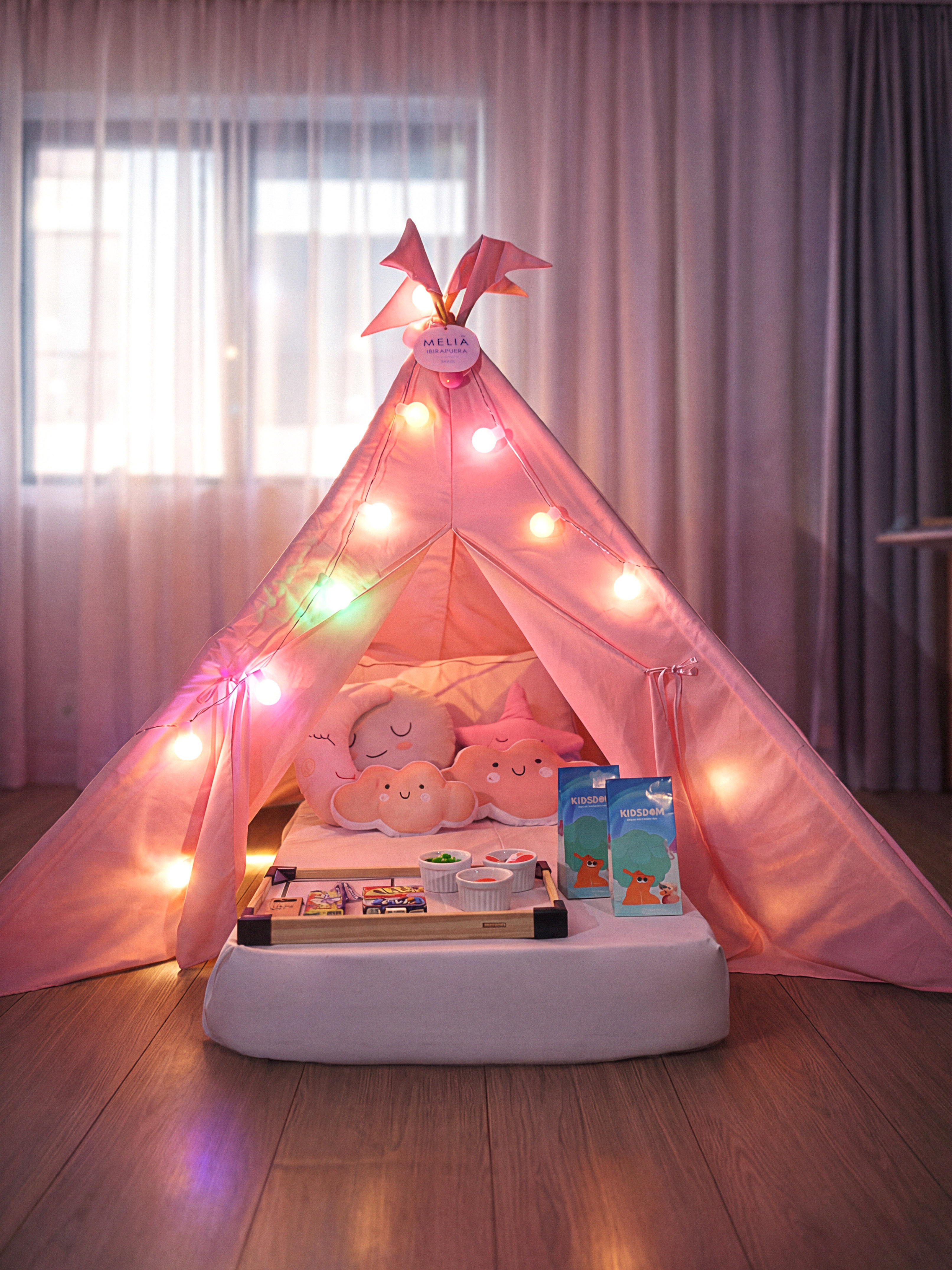 Pink Melia kids' play tent with string lights, pillows, and snack tray.