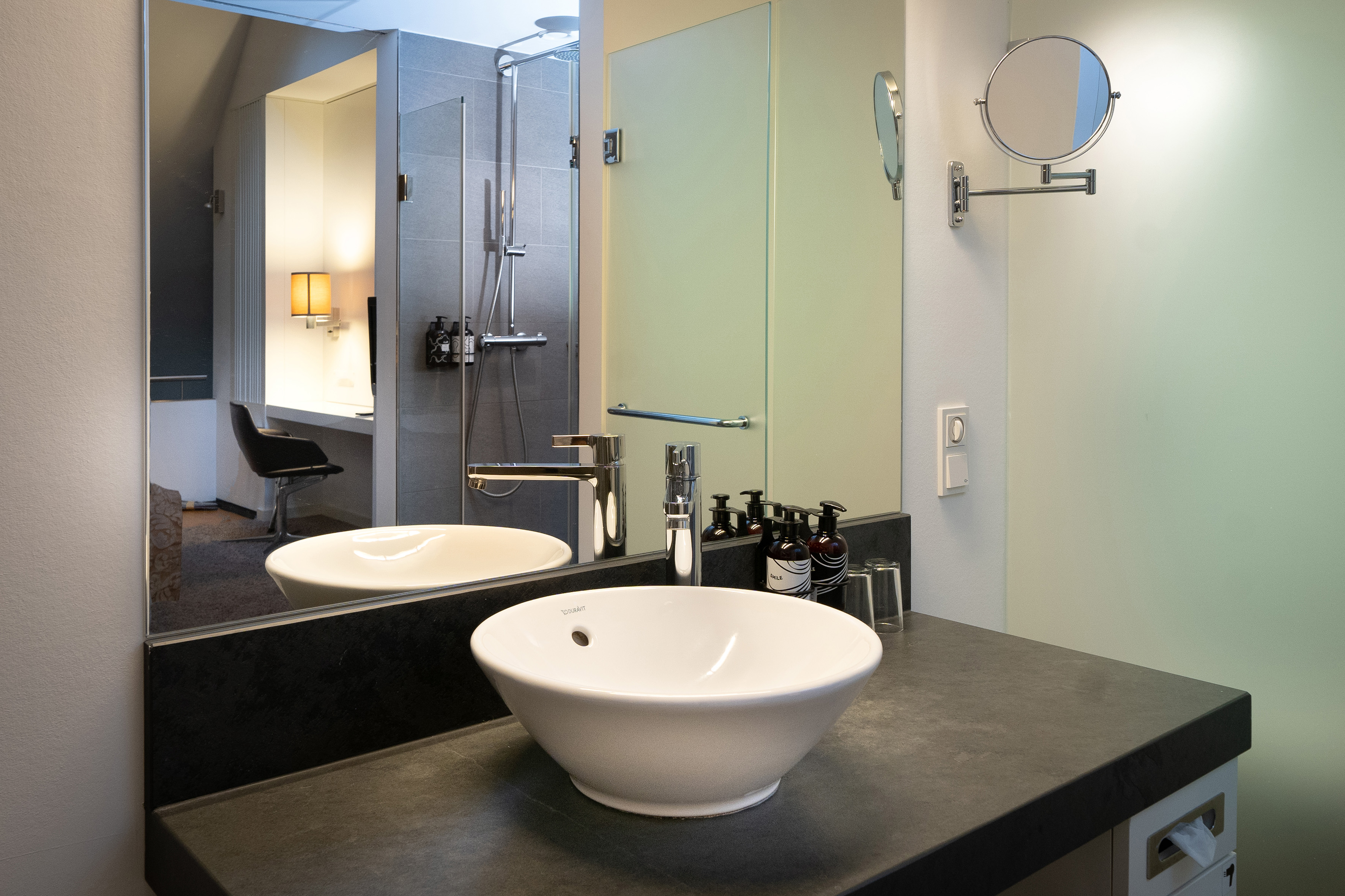 Modern hotel bathroom vanity with vessel sink, dark counter, and large mirror.