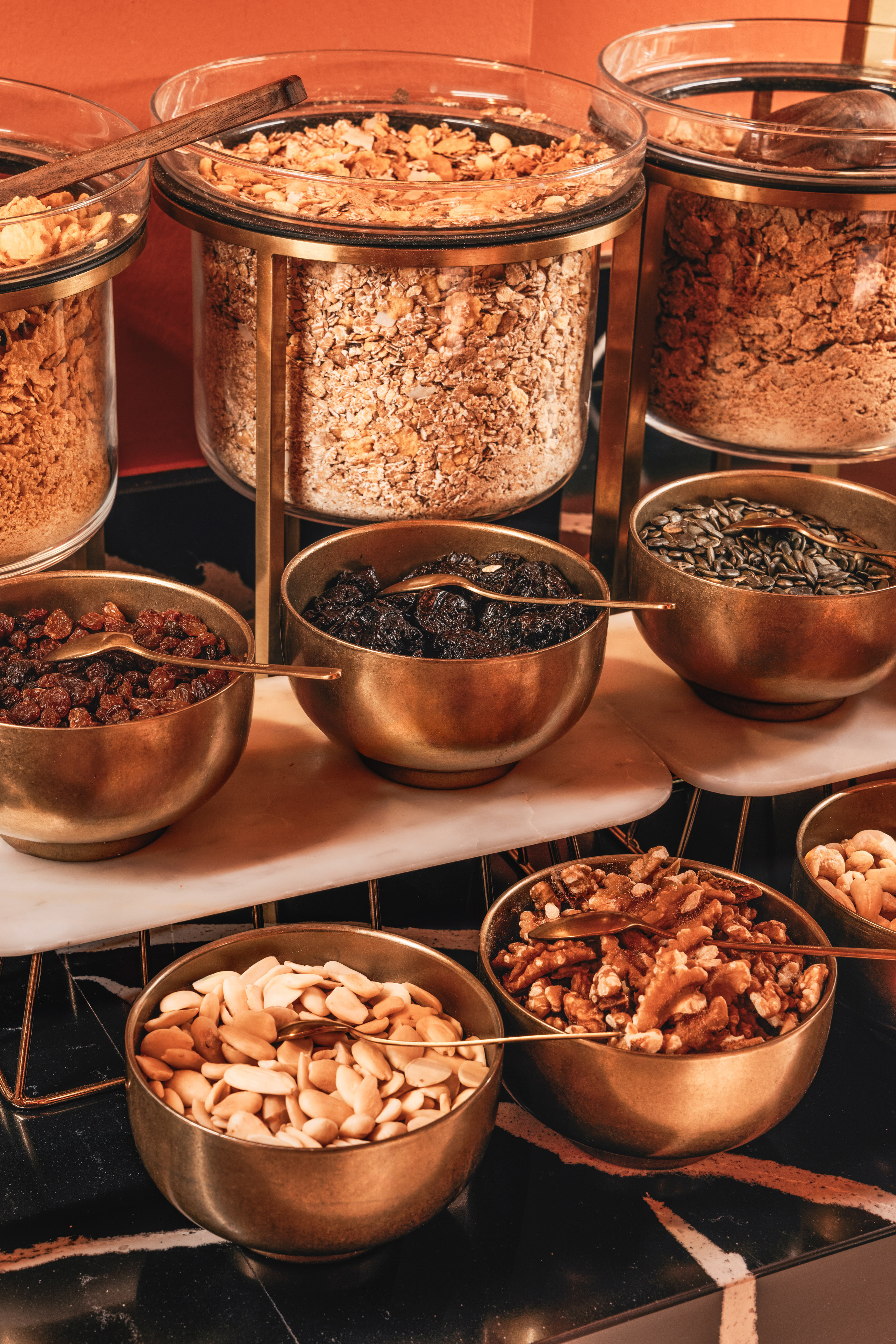 Breakfast buffet with cereals, granola, nuts, and dried fruit in brass bowls.