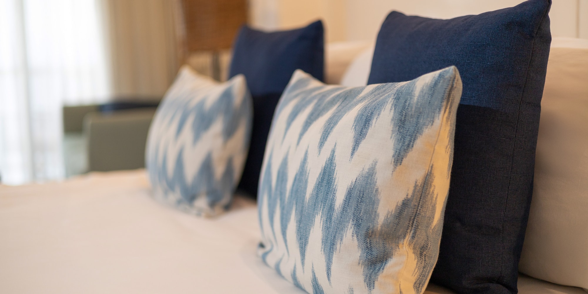 Blue and white ikat accent pillows on a neatly made bed with white linens.