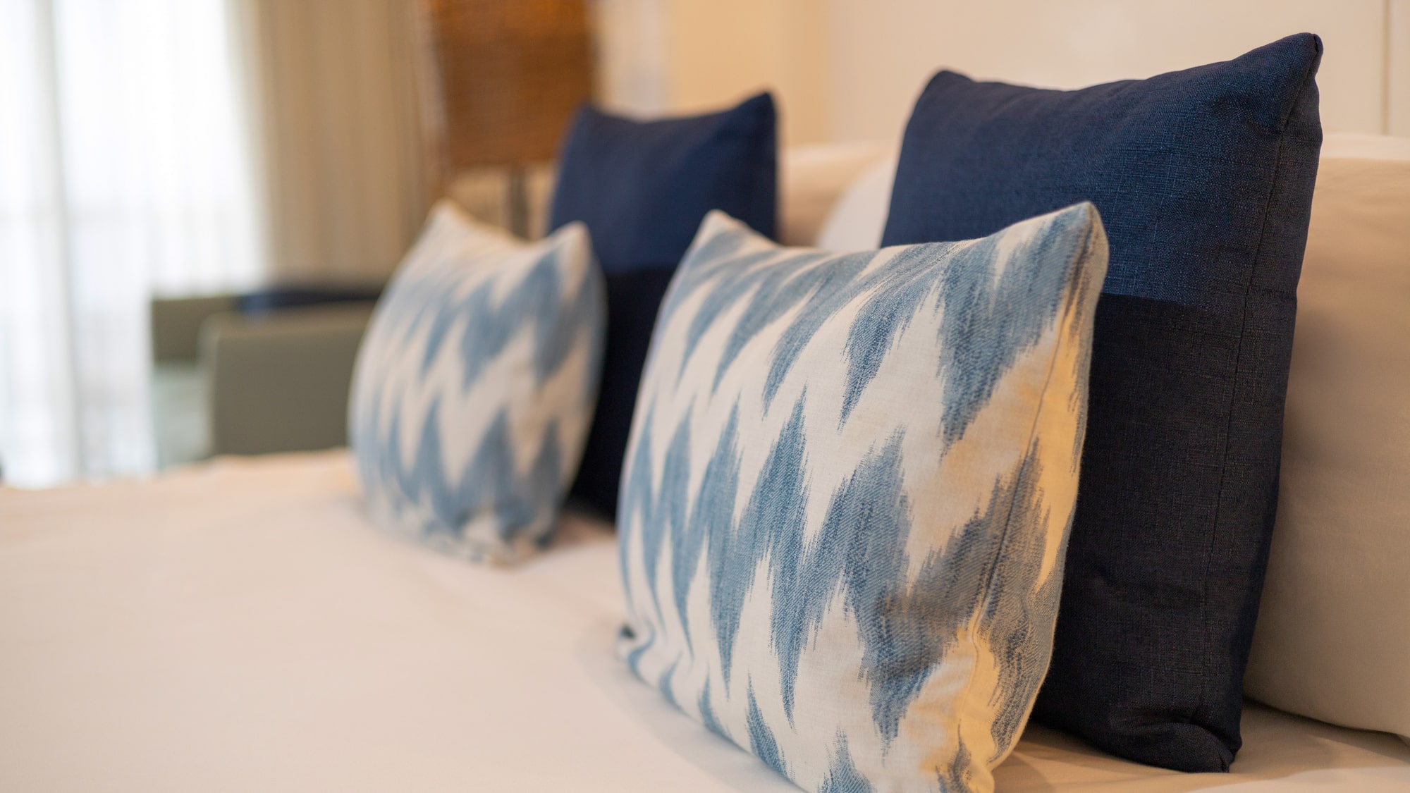 Blue and white ikat accent pillows on a neatly made bed with white linens.