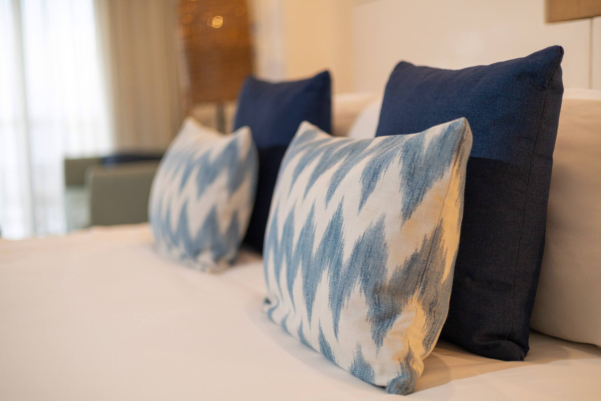 Blue and white ikat accent pillows on a neatly made bed with white linens.