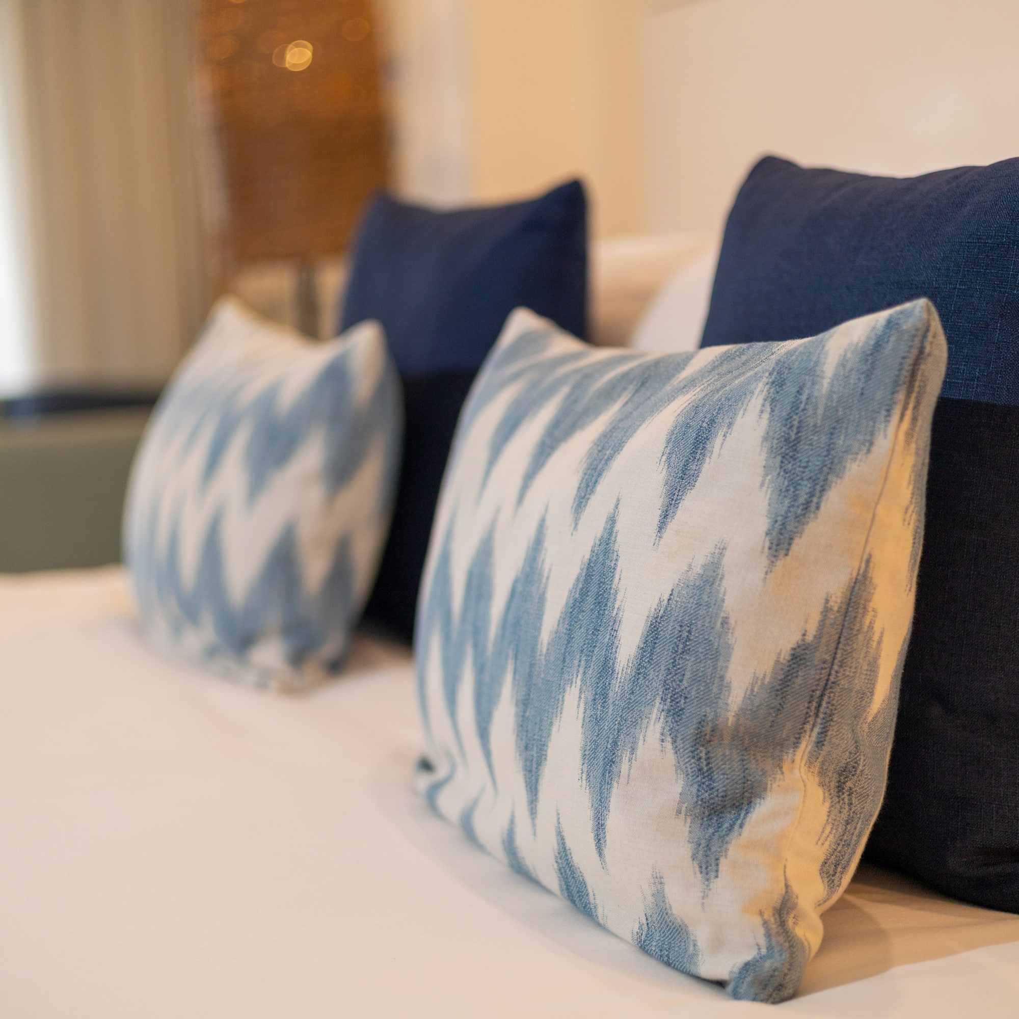 Blue and white ikat accent pillows on a neatly made bed with white linens.