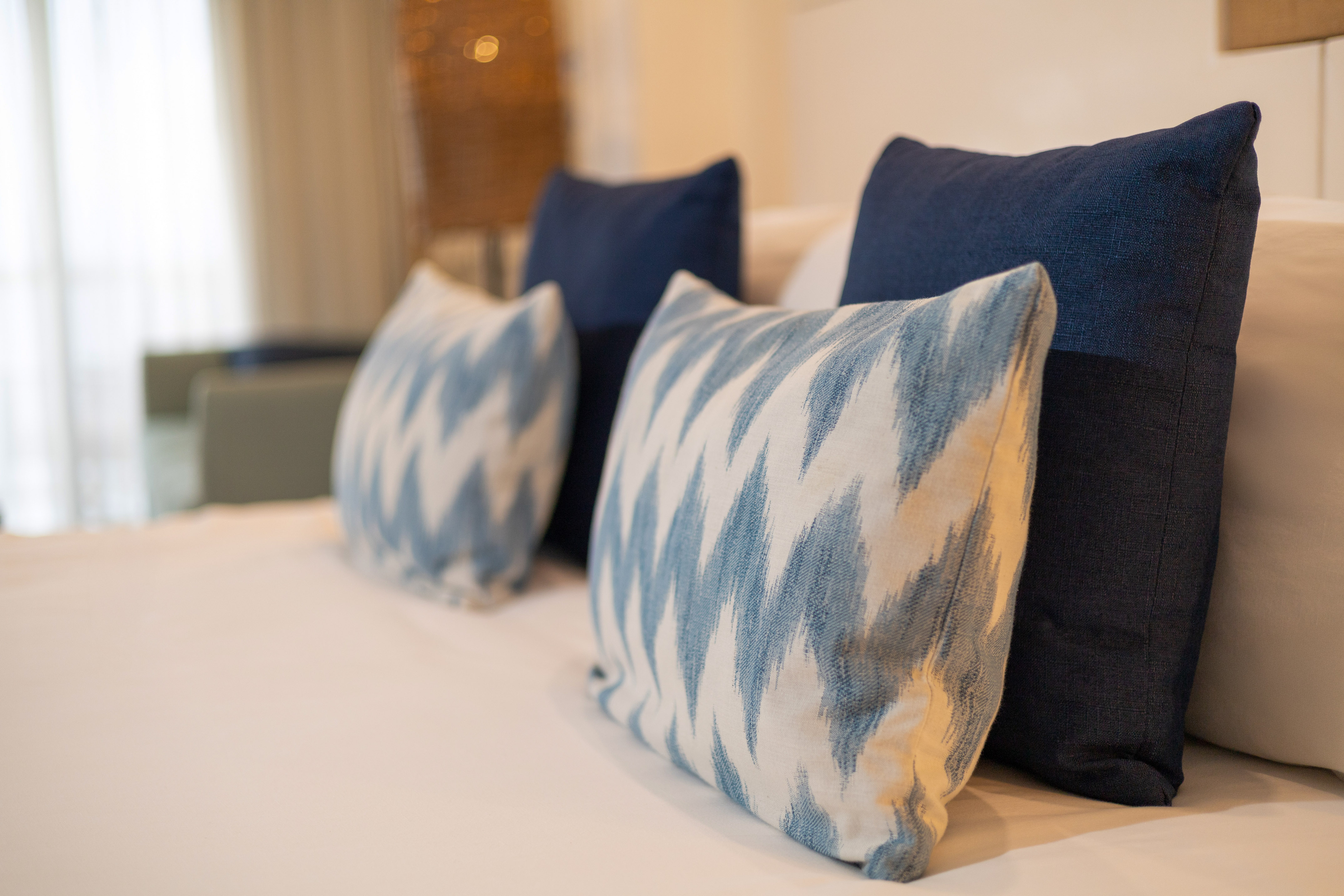 Blue and white ikat accent pillows on a neatly made bed with white linens.