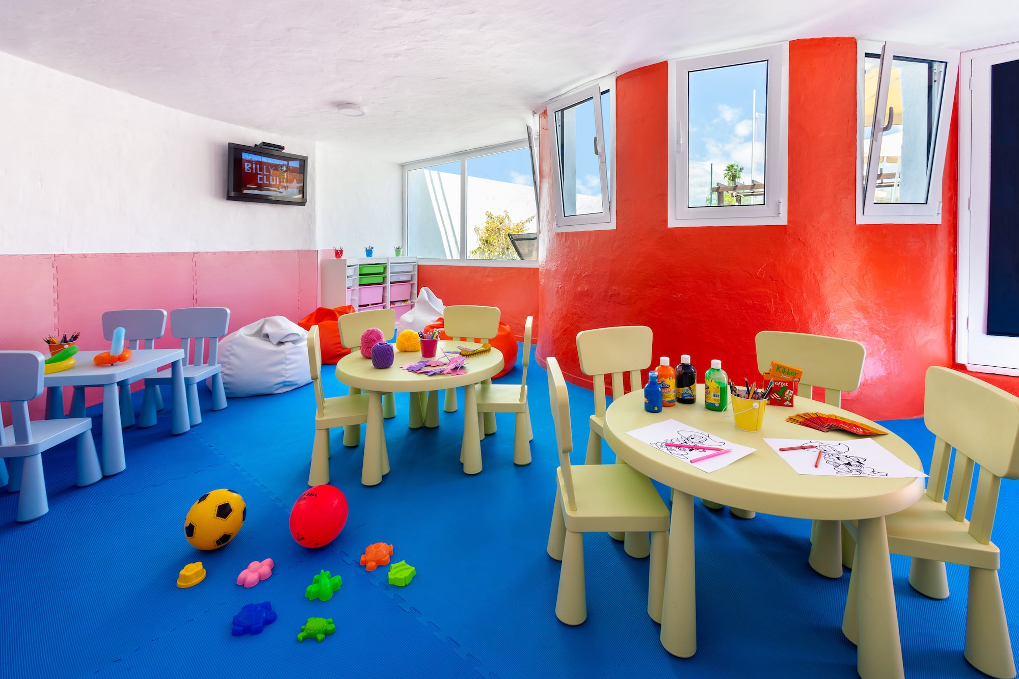 Colorful kids club play area with small tables, chairs, art supplies, and toys.