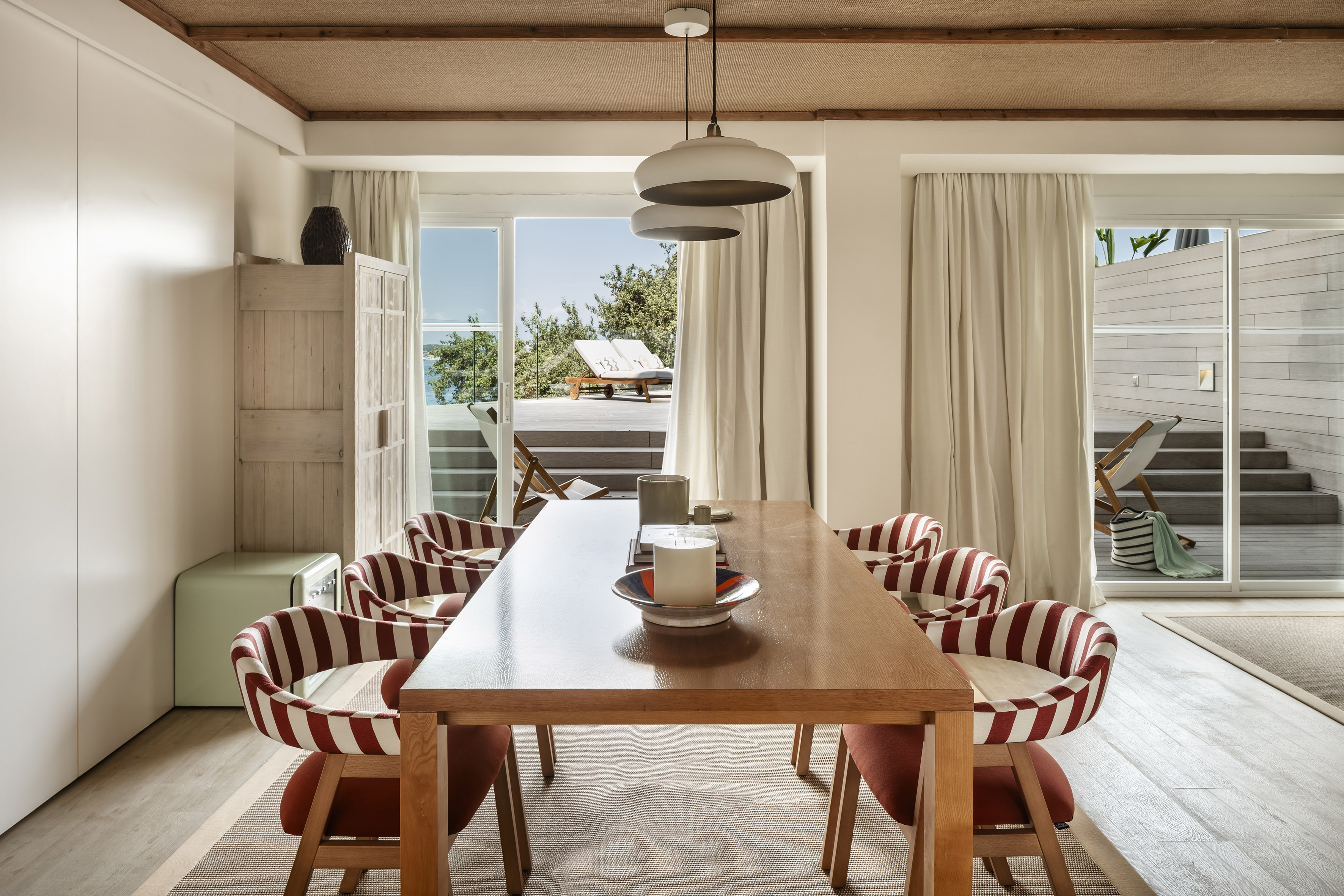 Coastal dining room with wooden table, red striped chairs, and ocean view deck.