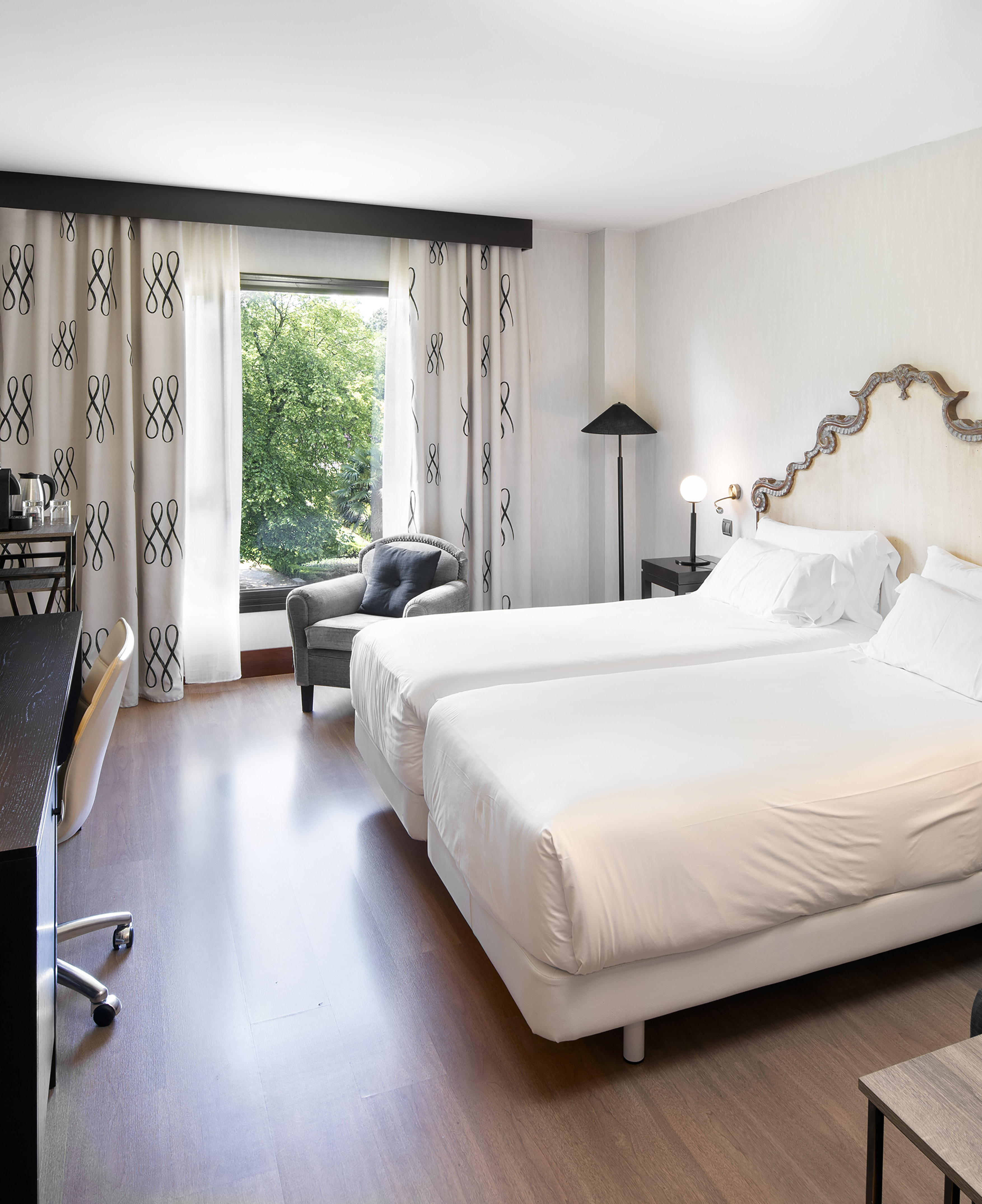 Bright hotel room with twin beds, desk, armchair, and garden view.