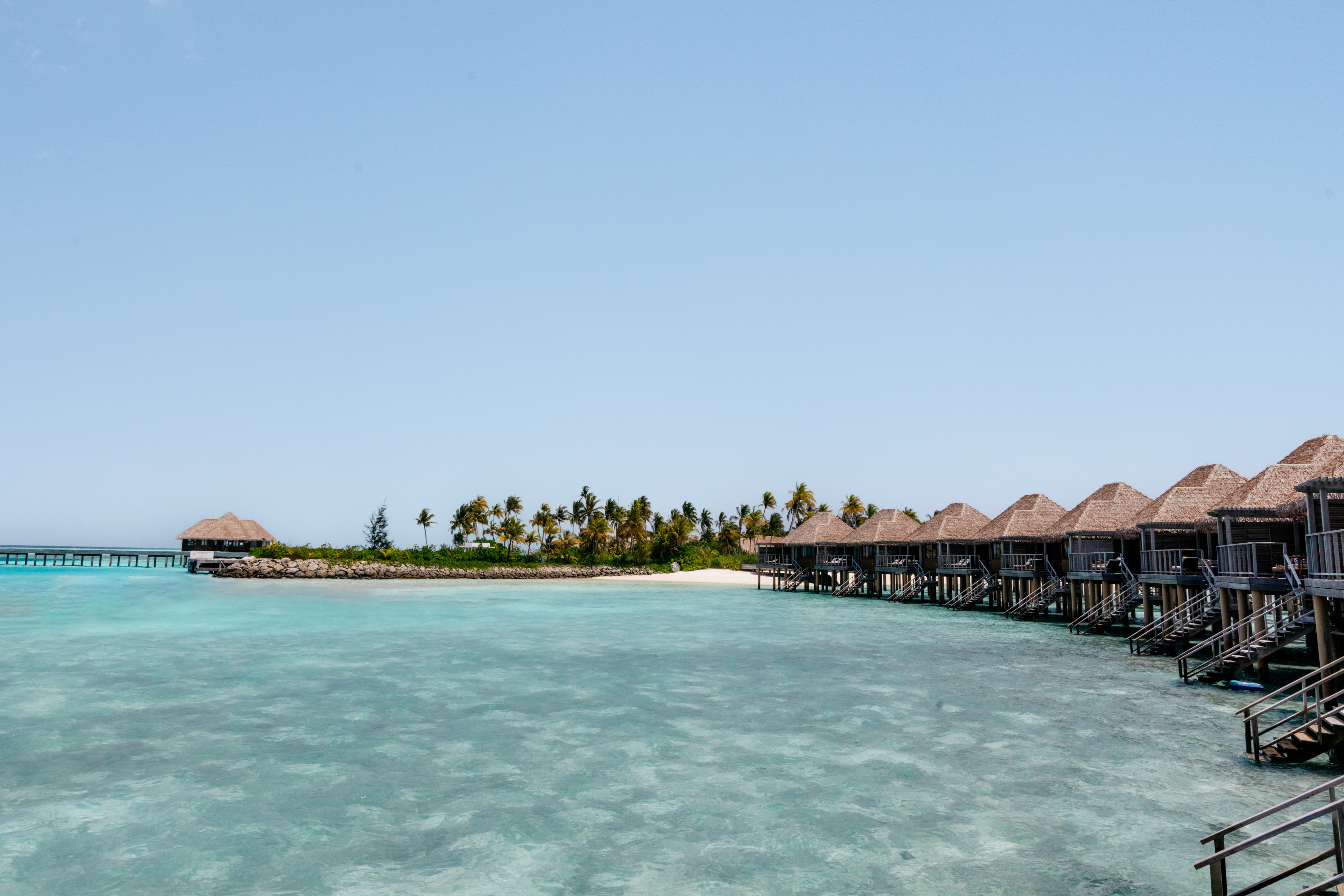Maldives overwater bungalows on turquoise water next to a palm-fringed island.