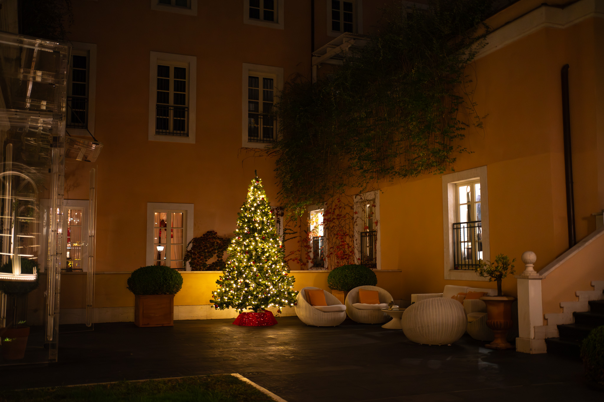 Brightly lit outdoor Christmas tree on a cozy building patio at night.