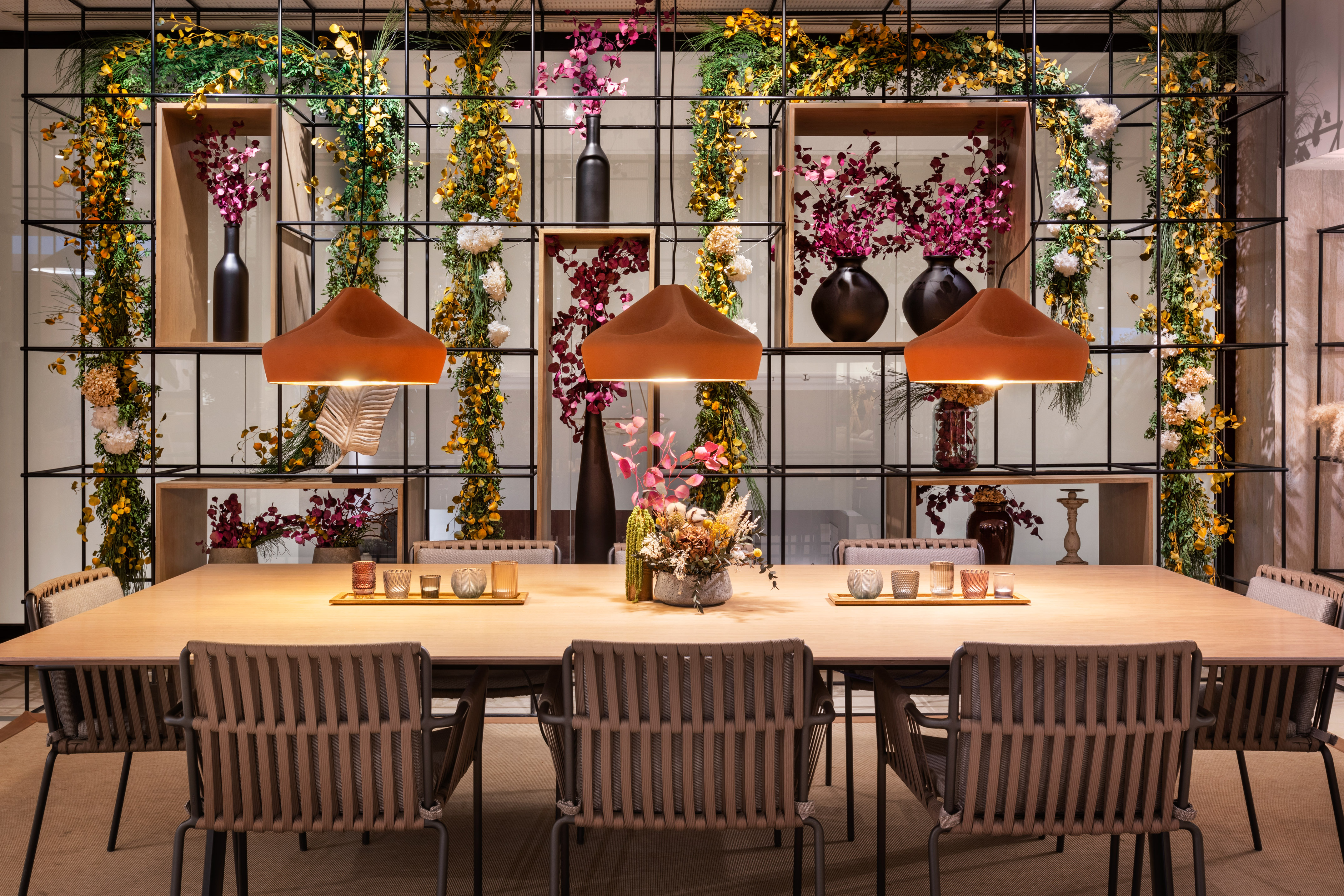 Modern dining room: wooden table, woven chairs, orange pendant lights, floral decor.