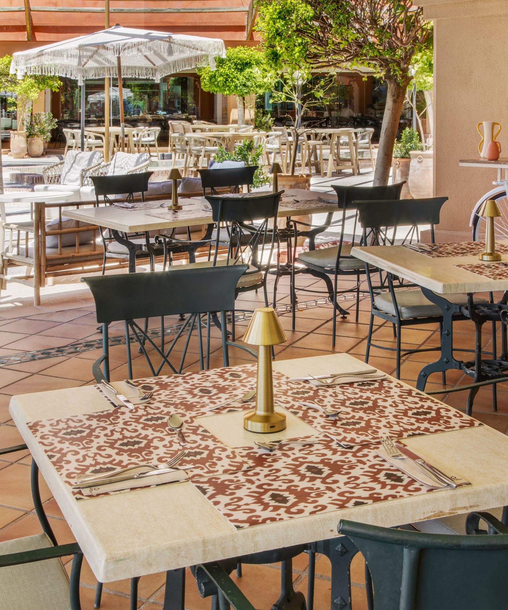 Outdoor restaurant patio with set dining tables, chairs, parasols, and greenery.