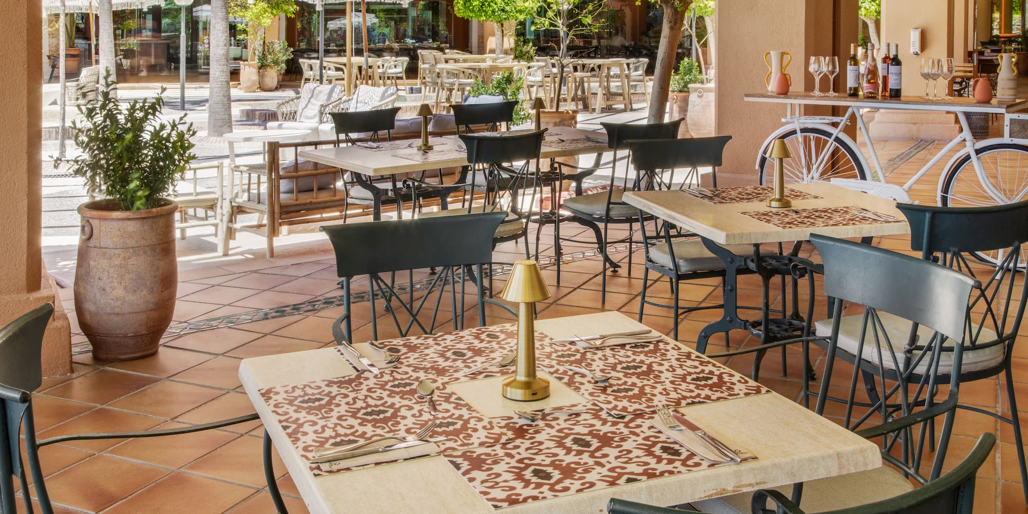 Outdoor restaurant patio with set dining tables, chairs, parasols, and greenery.