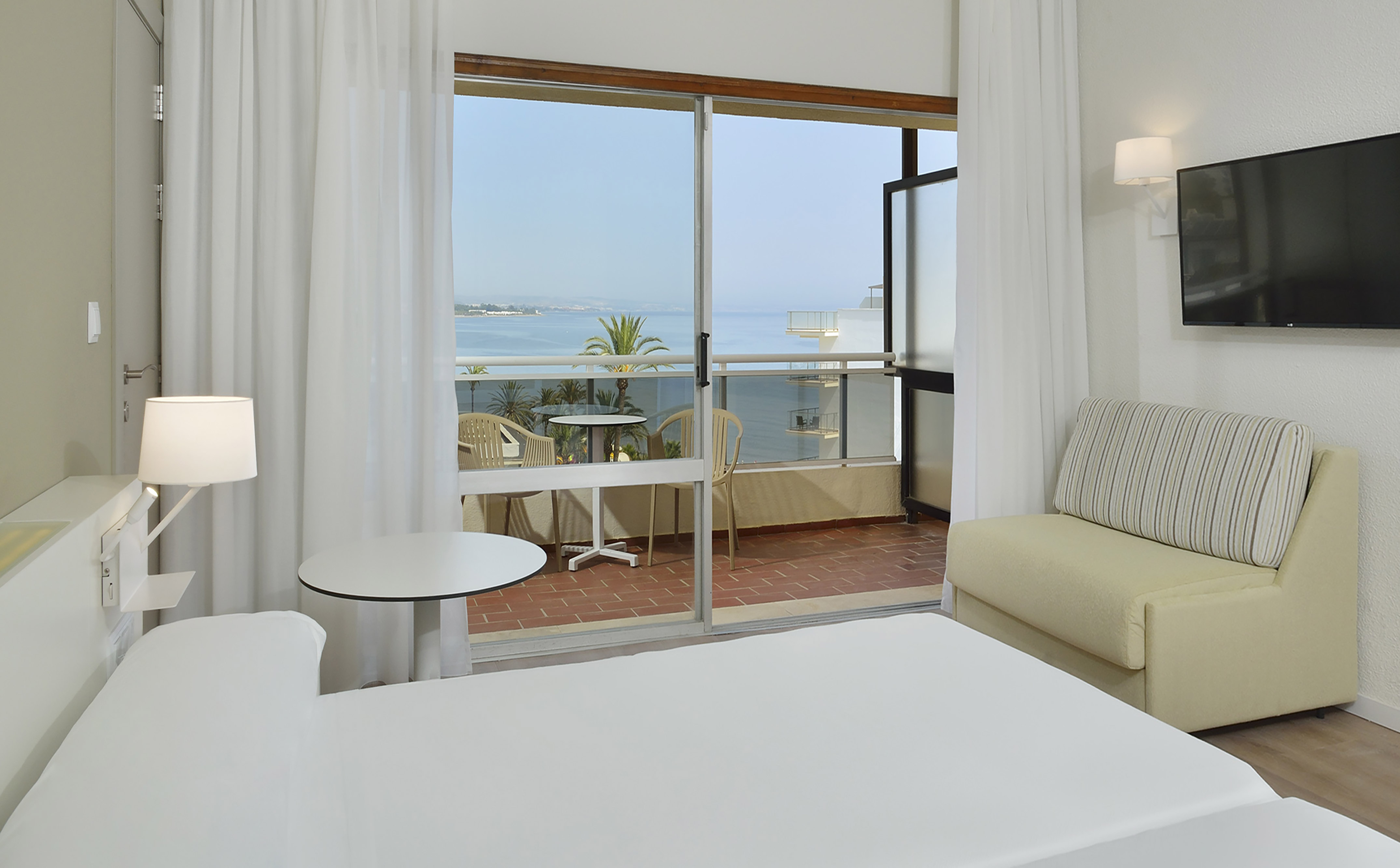 Hotel room with ocean view balcony, bed, and living area.
