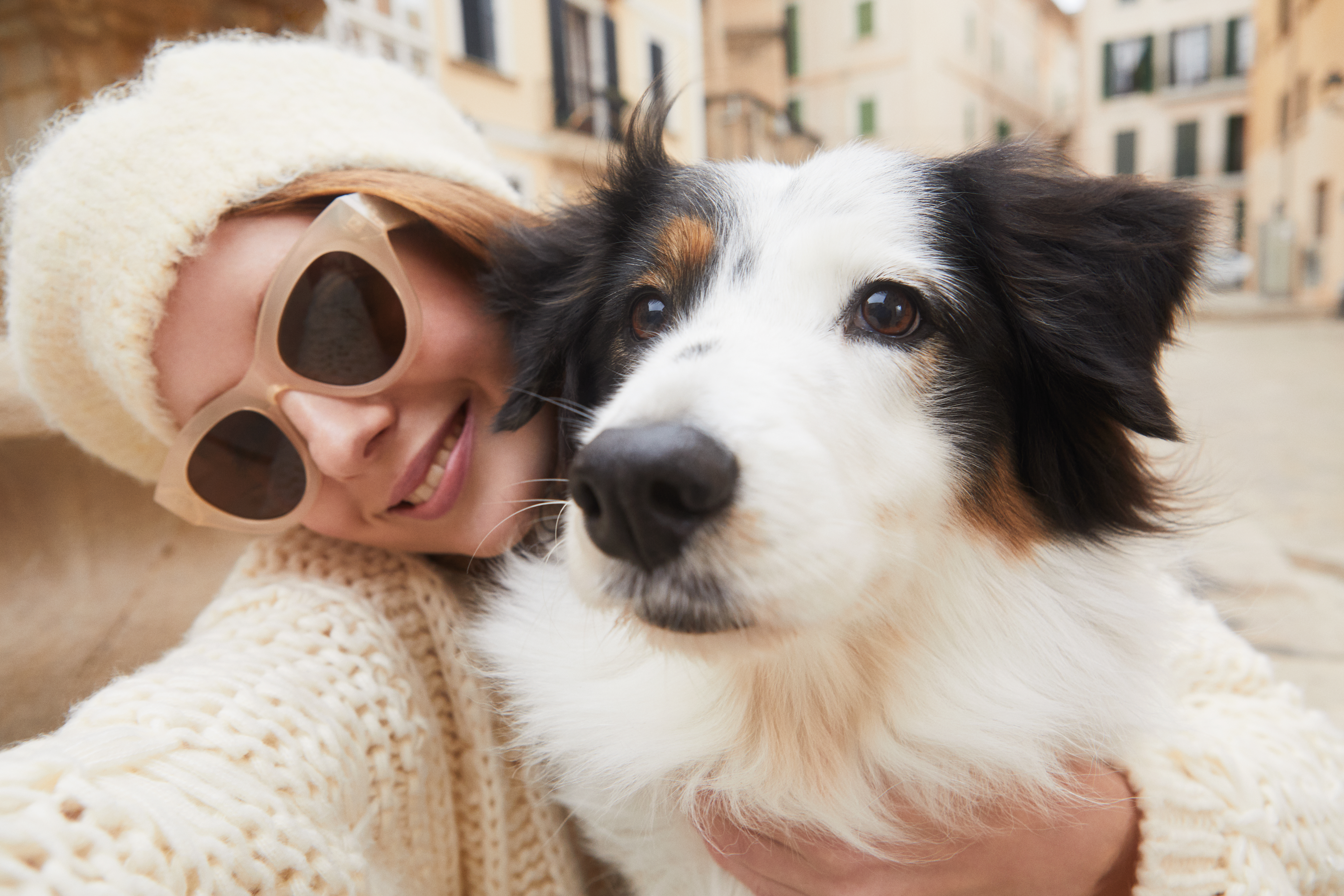 Woman in sunglasses and hat with tri-color dog selfie outdoors.