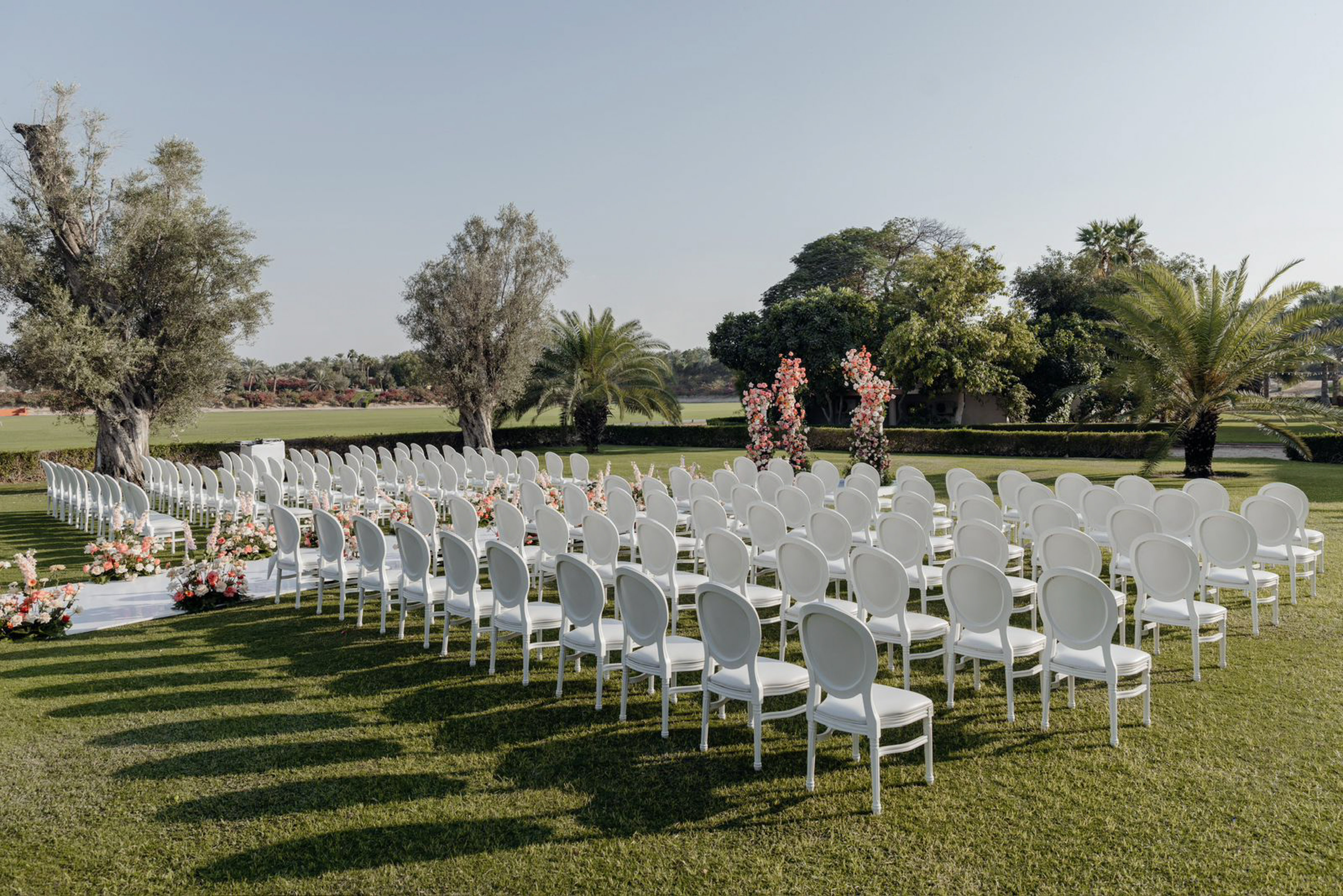 Outdoor wedding ceremony: white chairs, floral aisle decor, and green lawn.