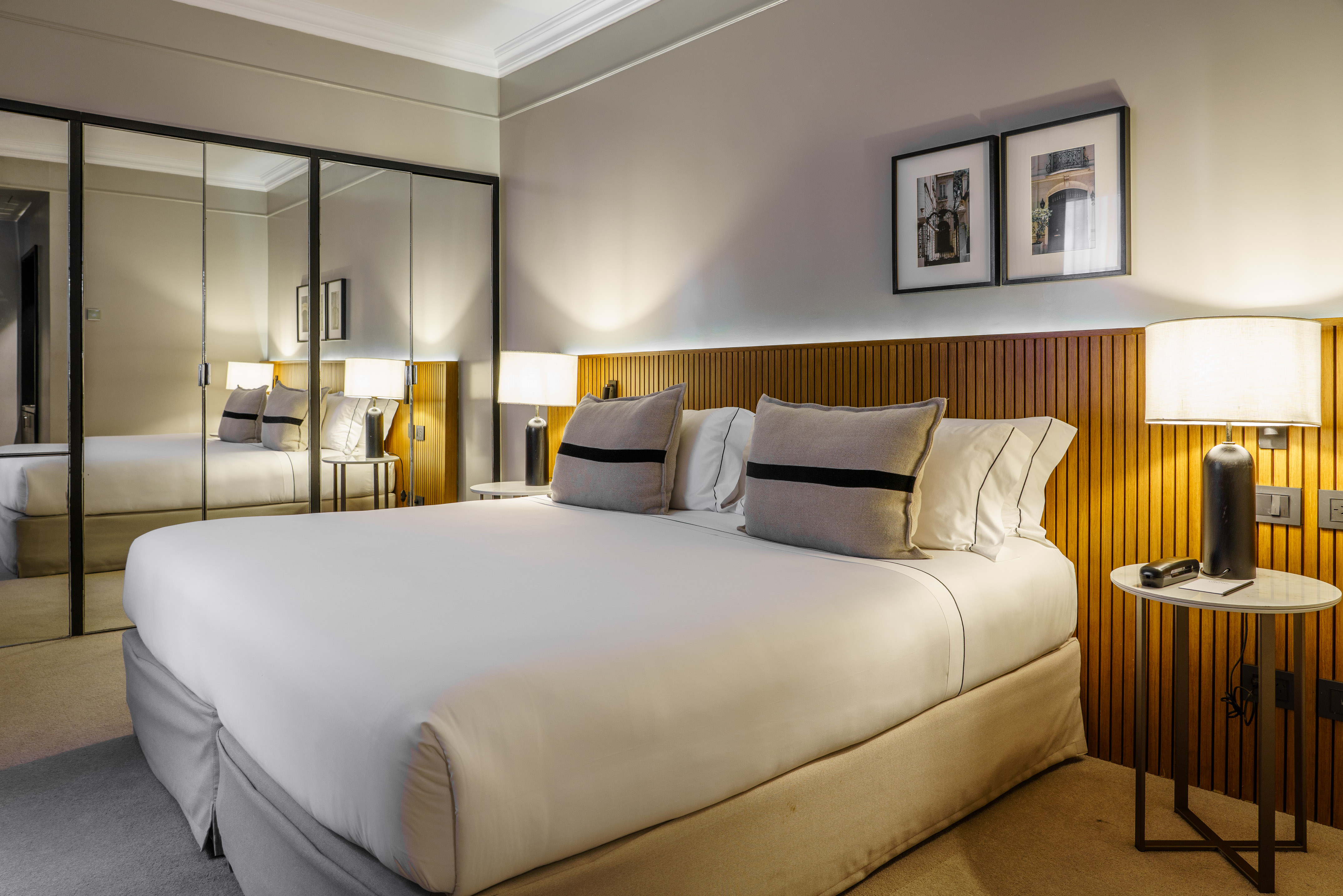 Modern hotel room with bed, wood headboard, bedside lamps, and mirrored wall.