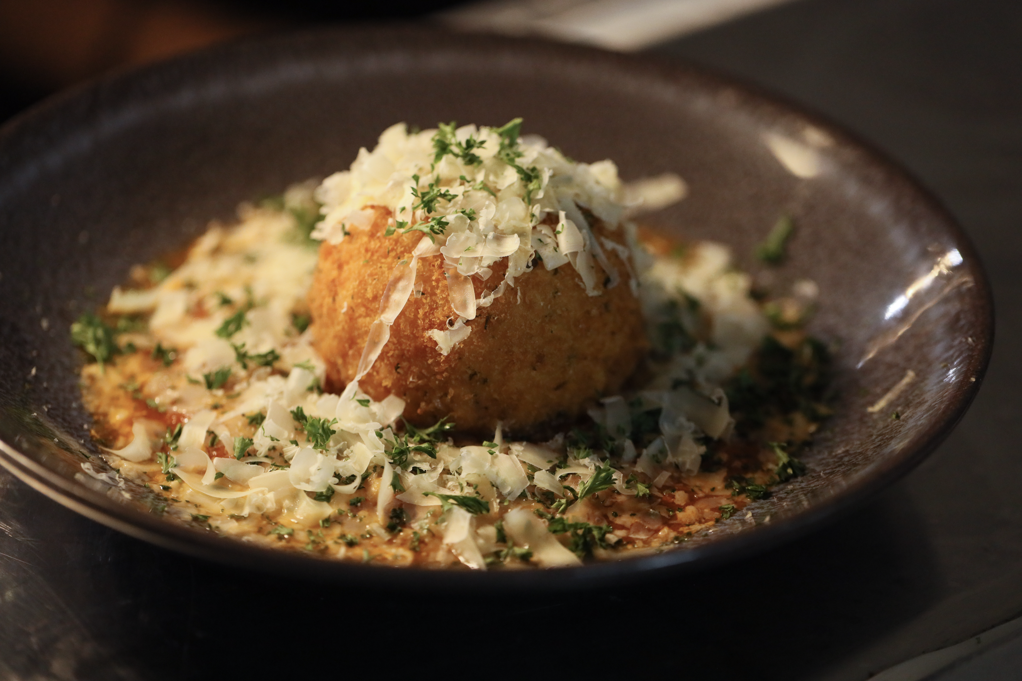 Golden arancini with shaved parmesan and fresh parsley in a rich sauce.