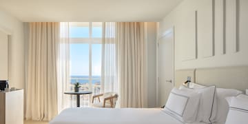 a room with two beds and a table with a view of the ocean