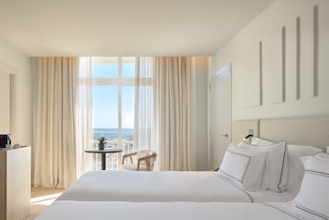 a room with two beds and a table with a view of the ocean