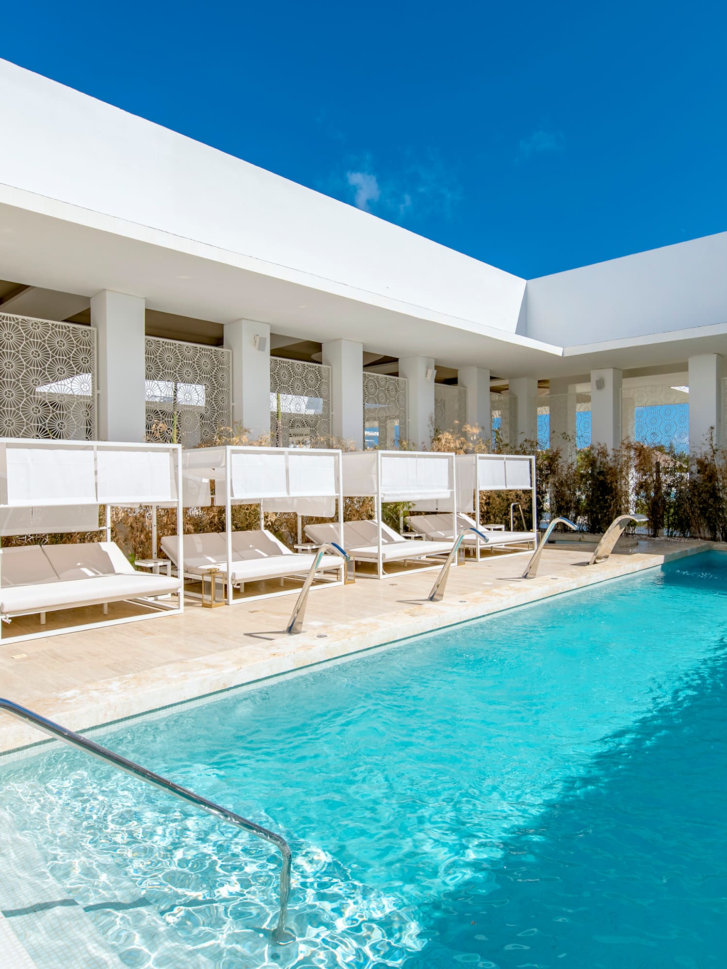 Modern outdoor luxury pool with white cabanas and geometric screens.
