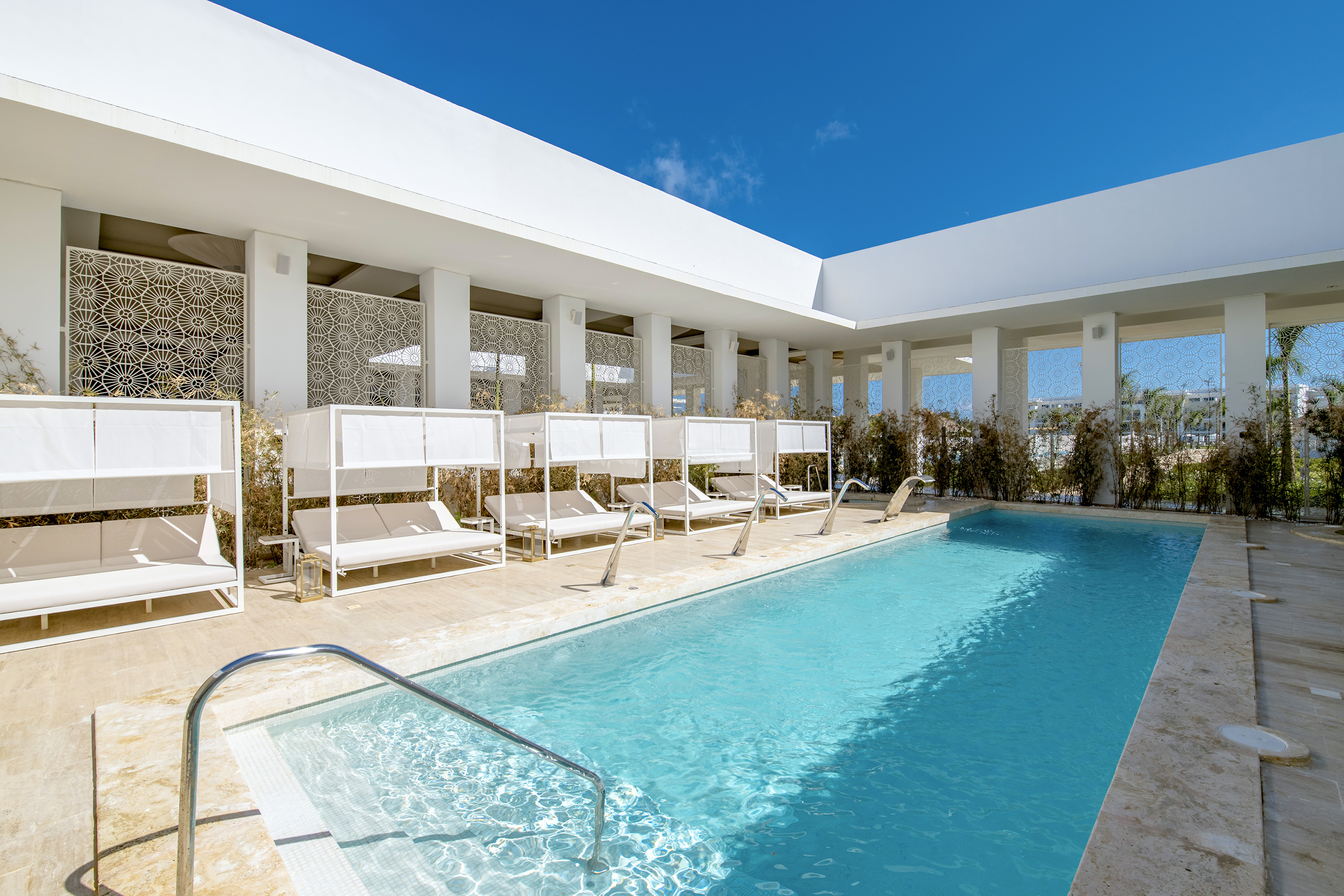 Modern outdoor luxury pool with white cabanas and geometric screens.