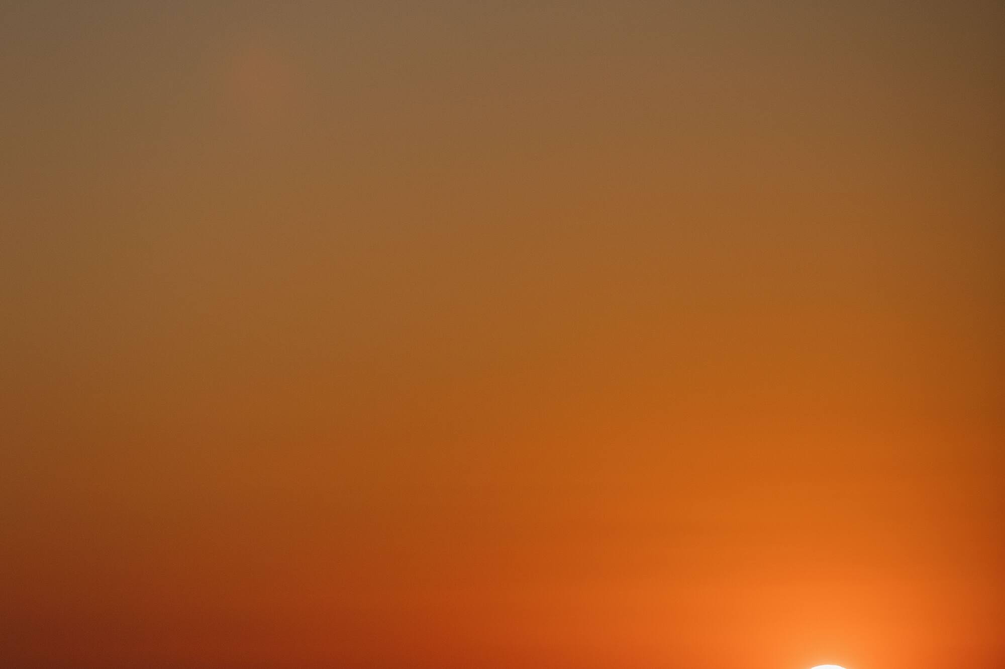 Vibrant orange sunset over dark ocean, with bright sun disk near the horizon.