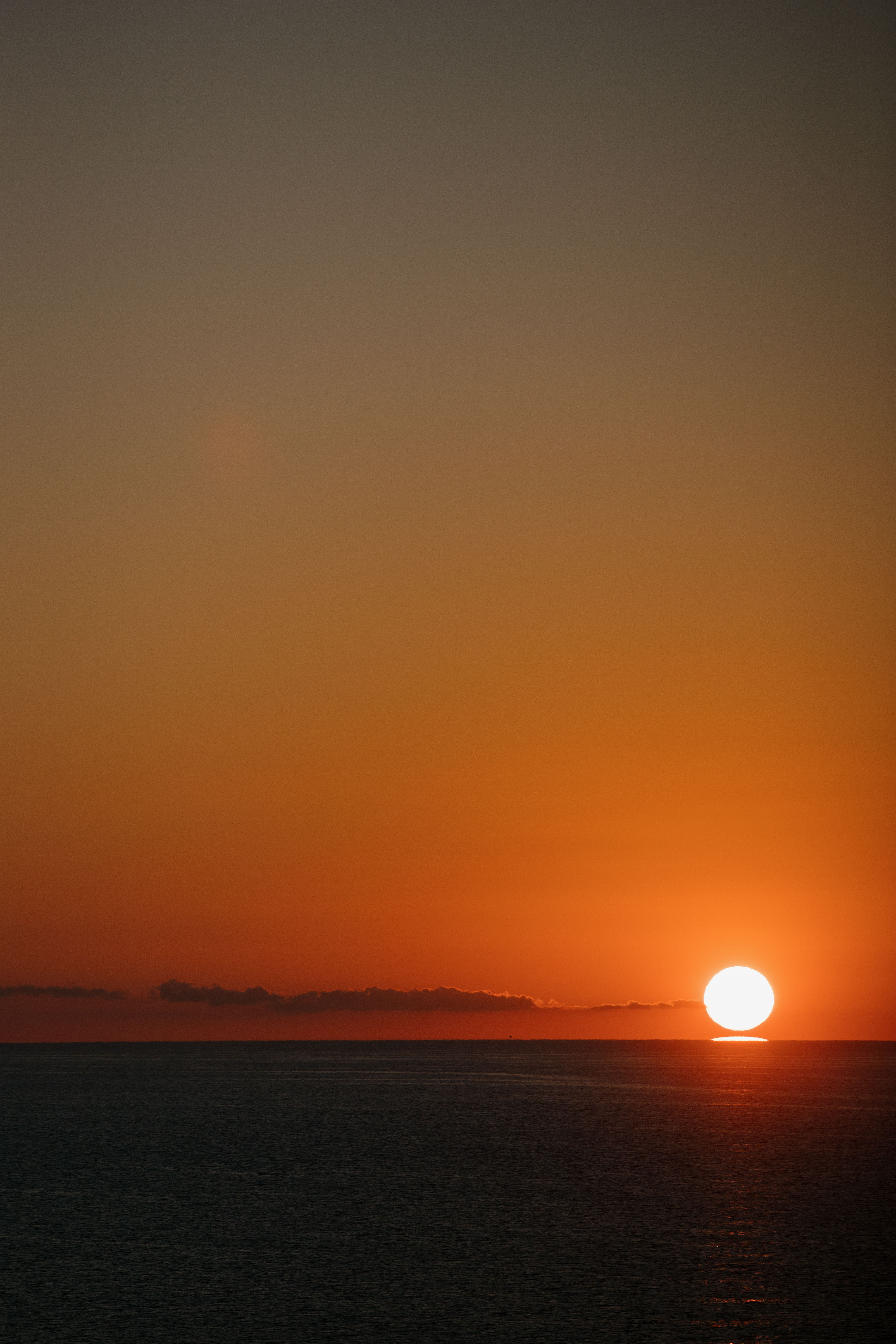 Vibrant orange sunset over dark ocean, with bright sun disk near the horizon.