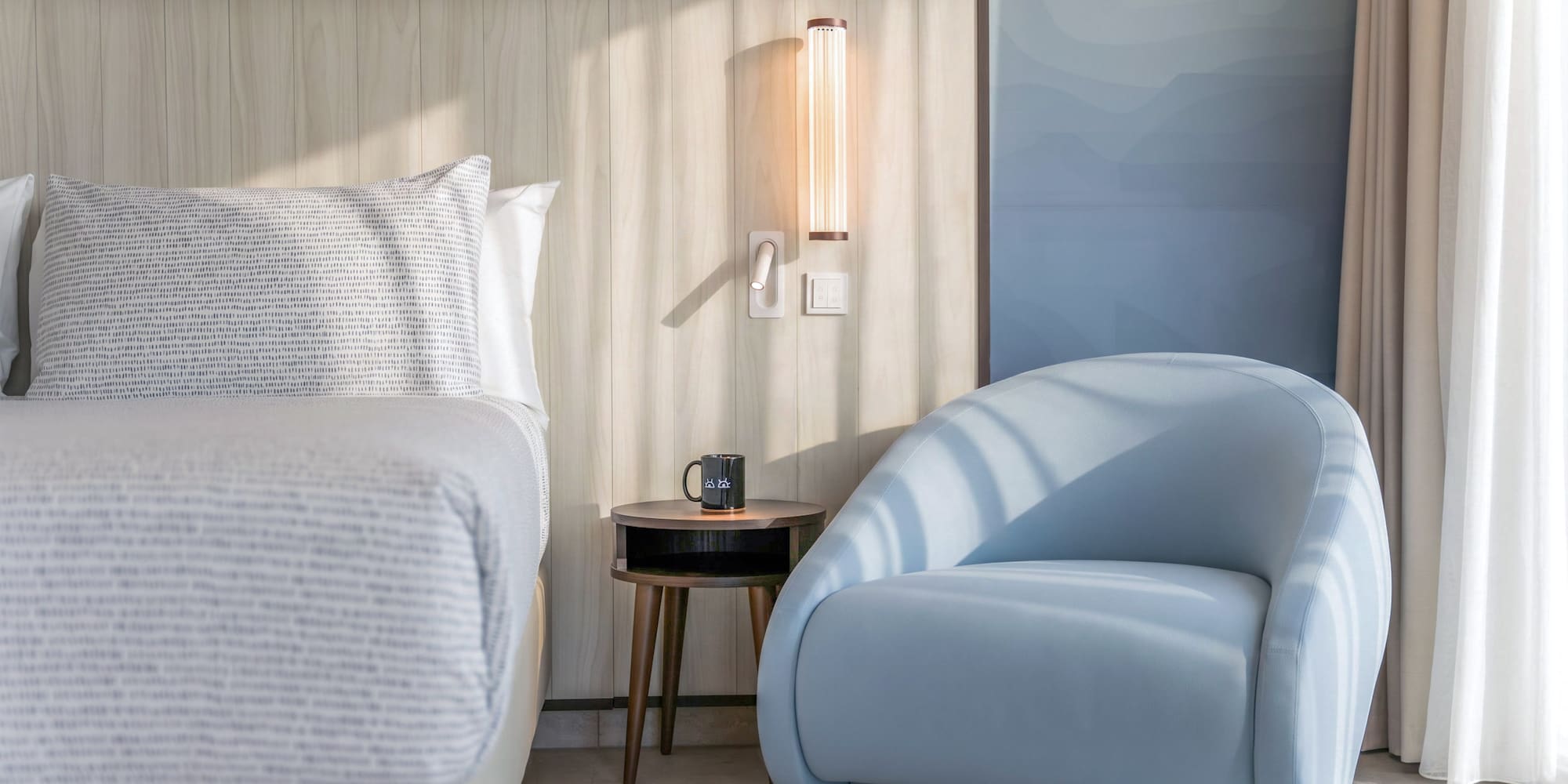 Modern hotel bedroom with light wood headboard and stylish blue armchair.