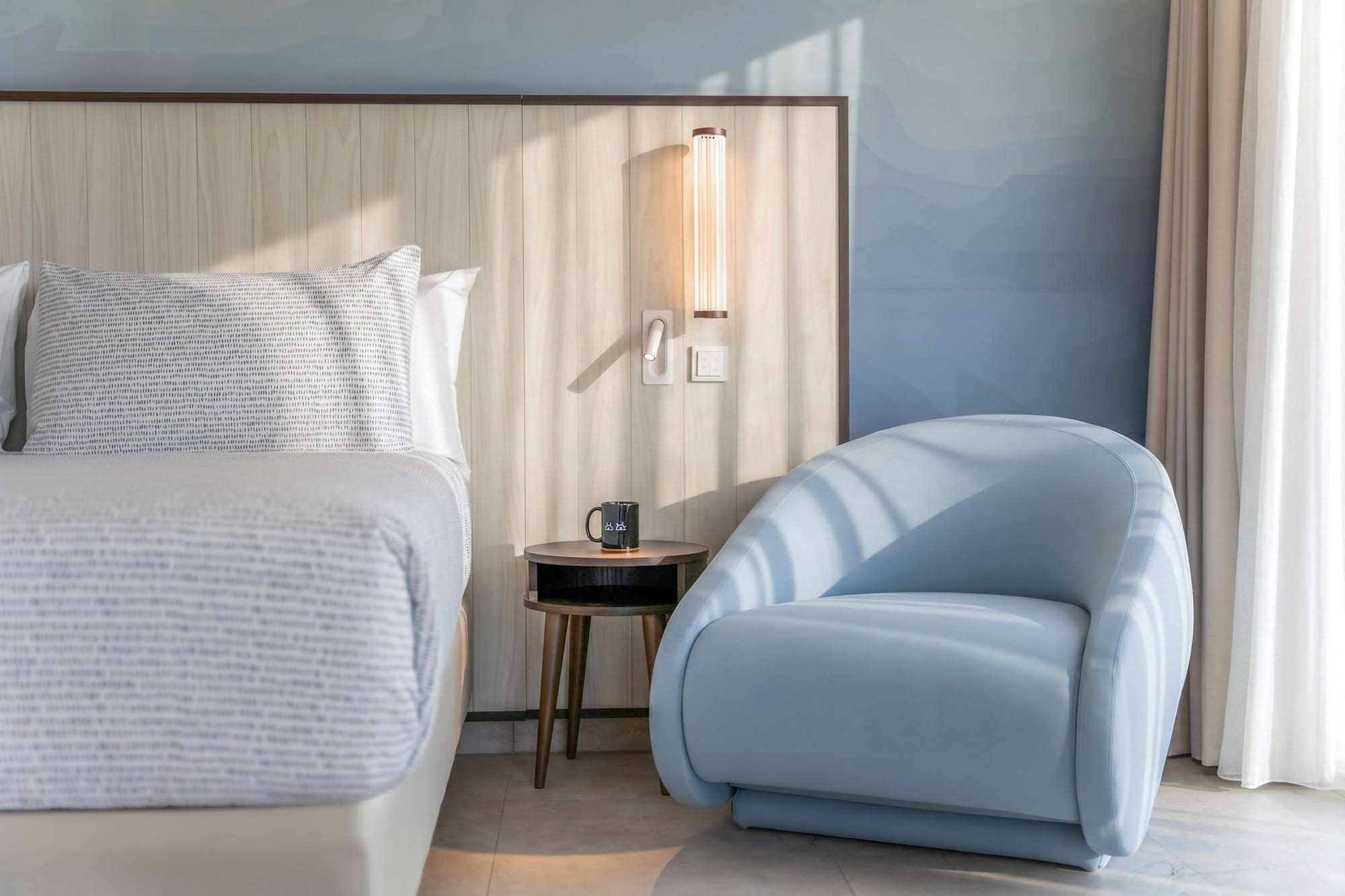 Modern hotel bedroom with light wood headboard and stylish blue armchair.