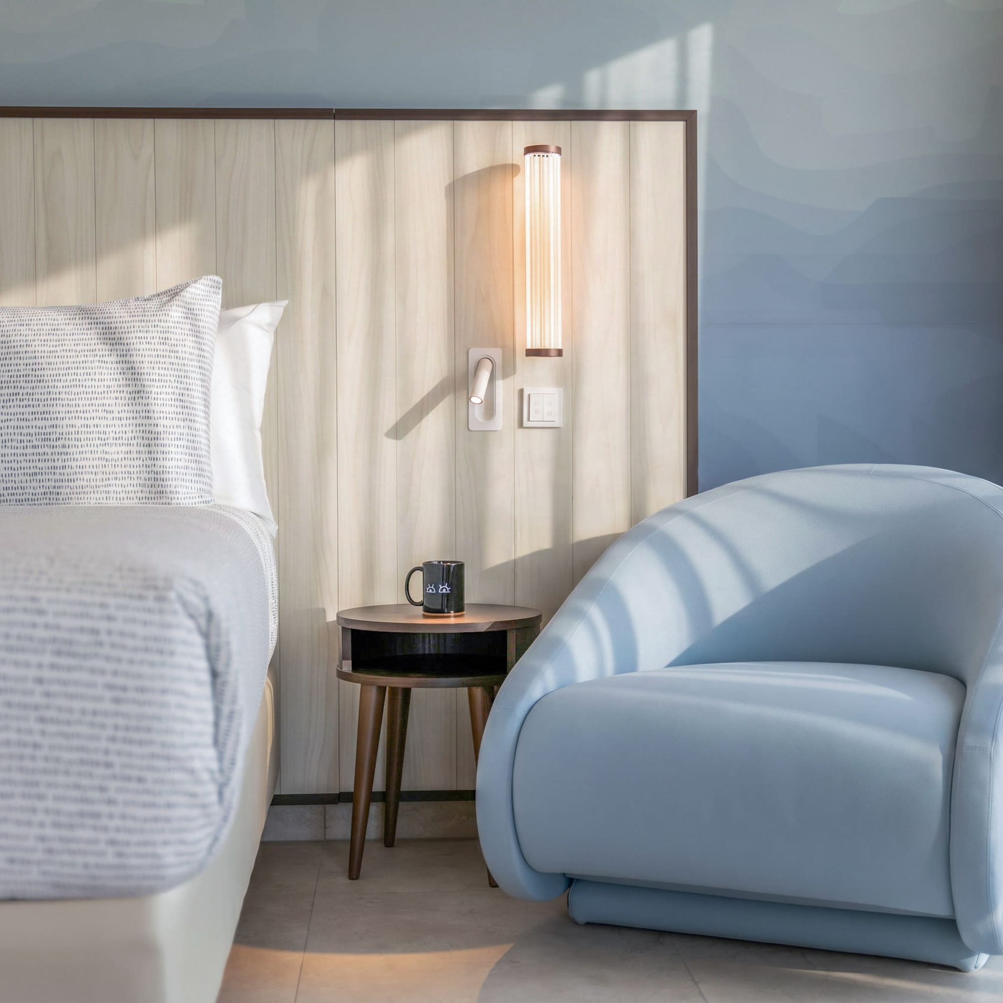Modern hotel bedroom with light wood headboard and stylish blue armchair.