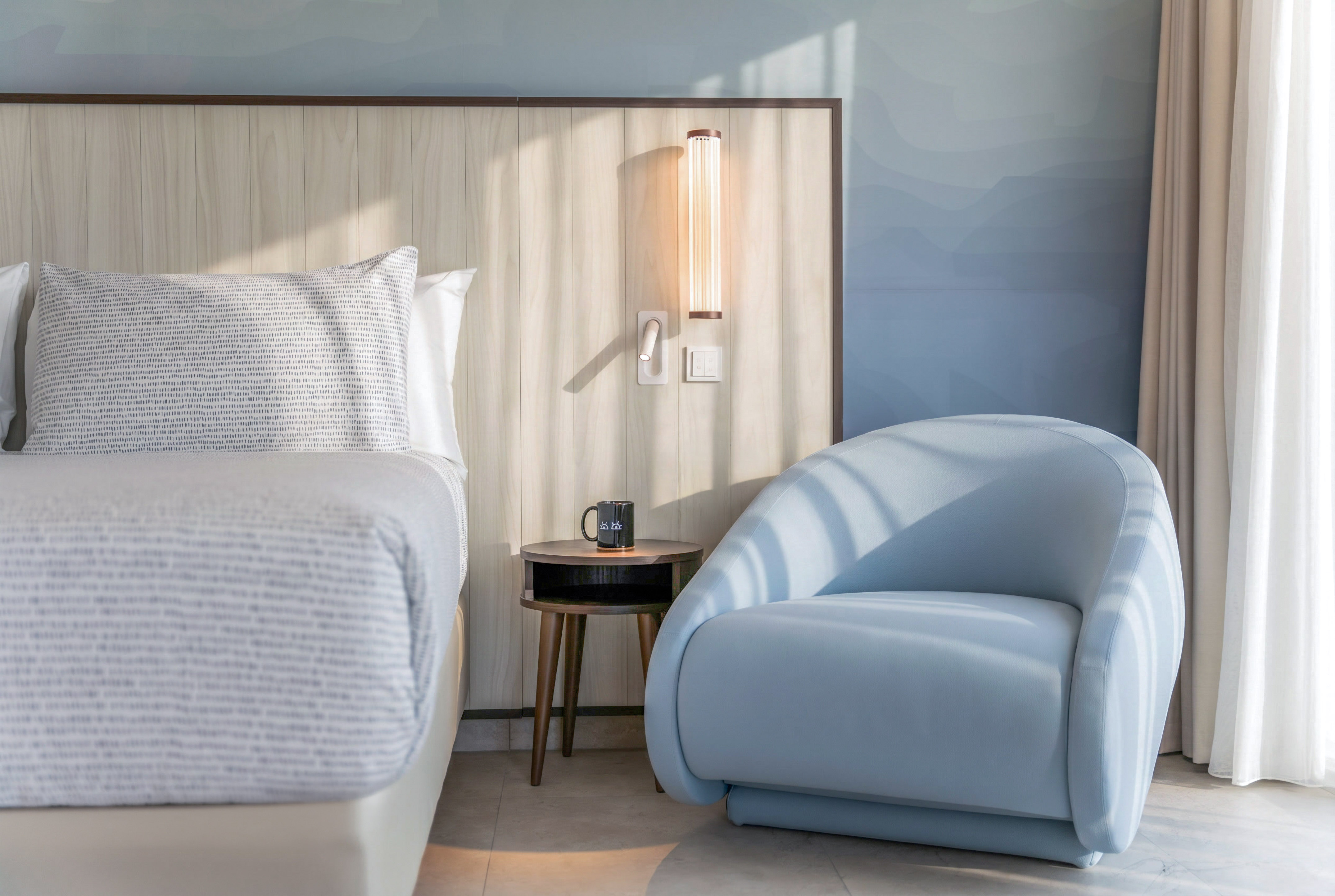 Modern hotel bedroom with light wood headboard and stylish blue armchair.