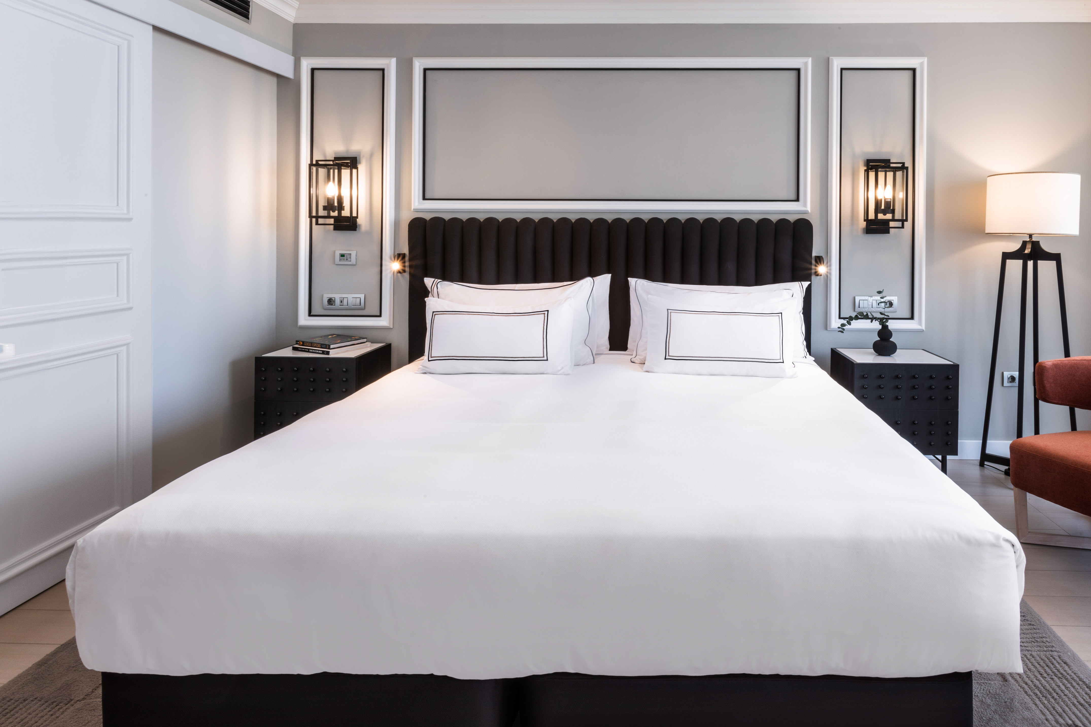 Elegant hotel bedroom with large white bed, black headboard, and modern lighting.