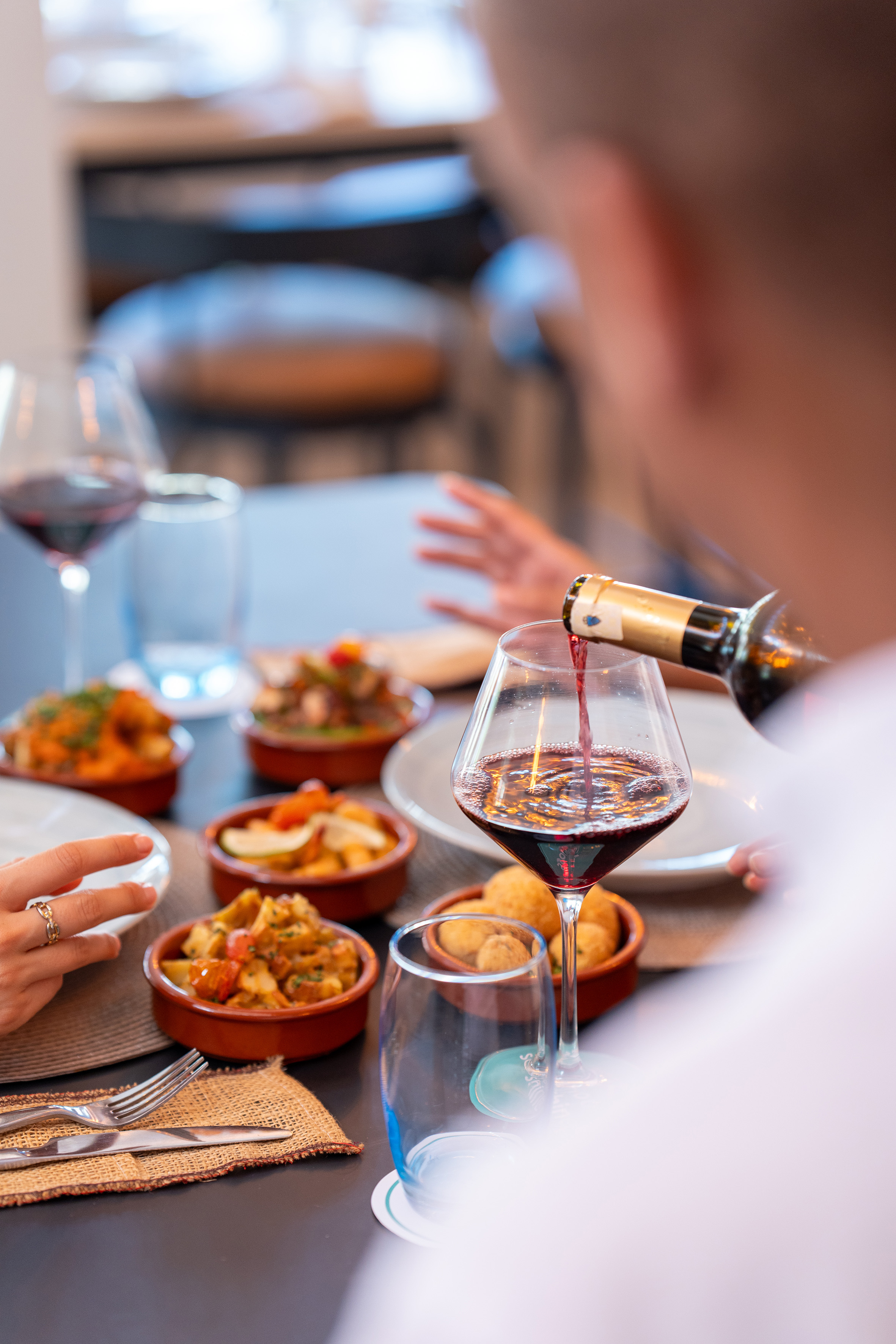 Pouring red wine into a glass at a restaurant table with diverse tapas dishes. - Restaurant Darna, Showkochen - SOL Oasis Marrakech, Marrakesch