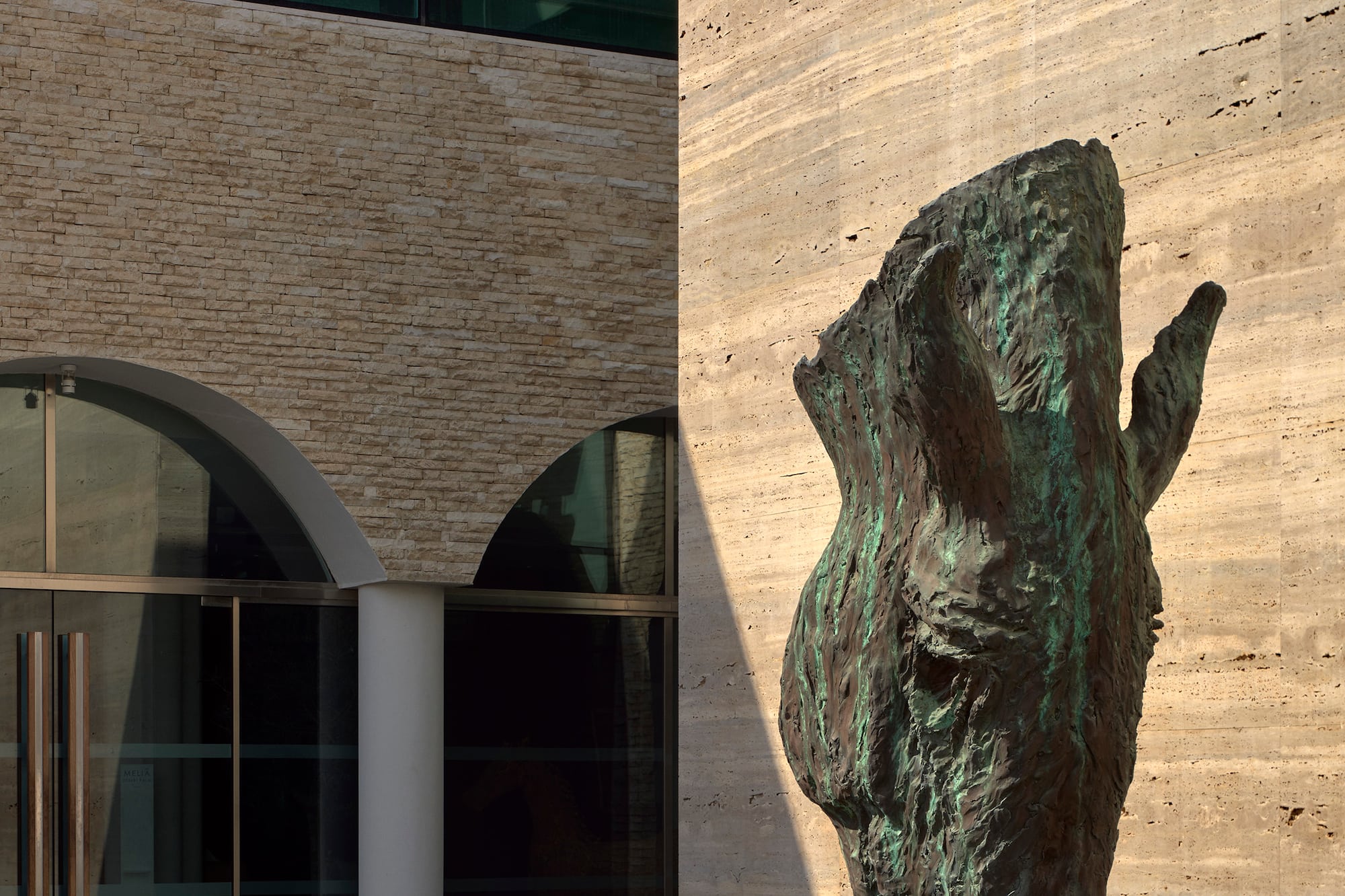 Abstract bronze sculpture in a modern fountain with a stone and glass building facade.