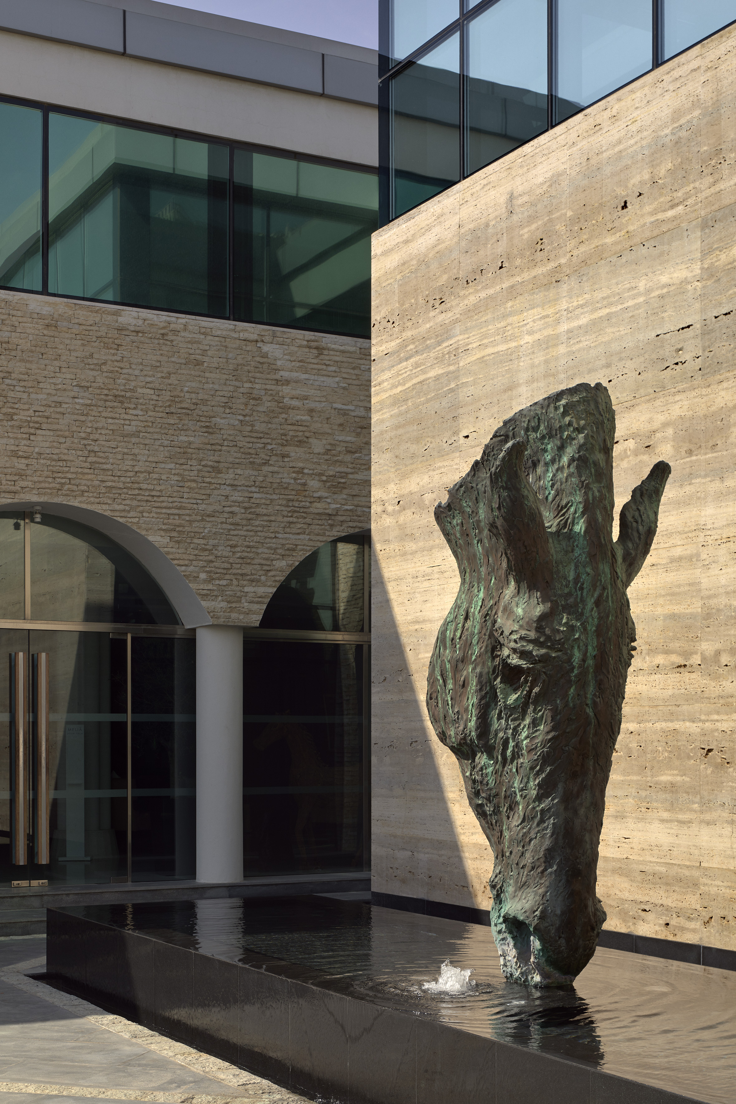 Abstract bronze sculpture in a modern fountain with a stone and glass building facade.