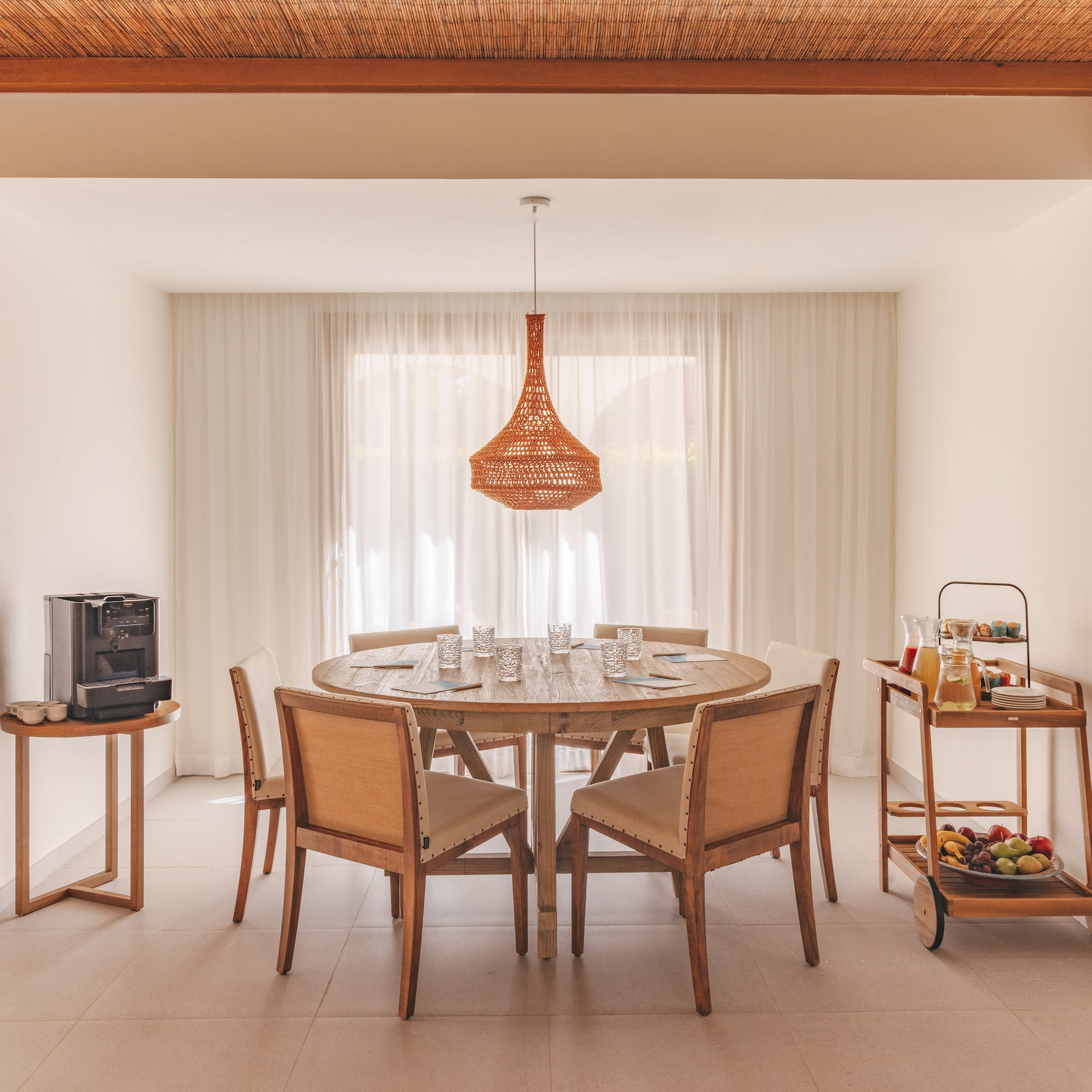 Dining area with wooden table, woven light, coffee, and breakfast cart.