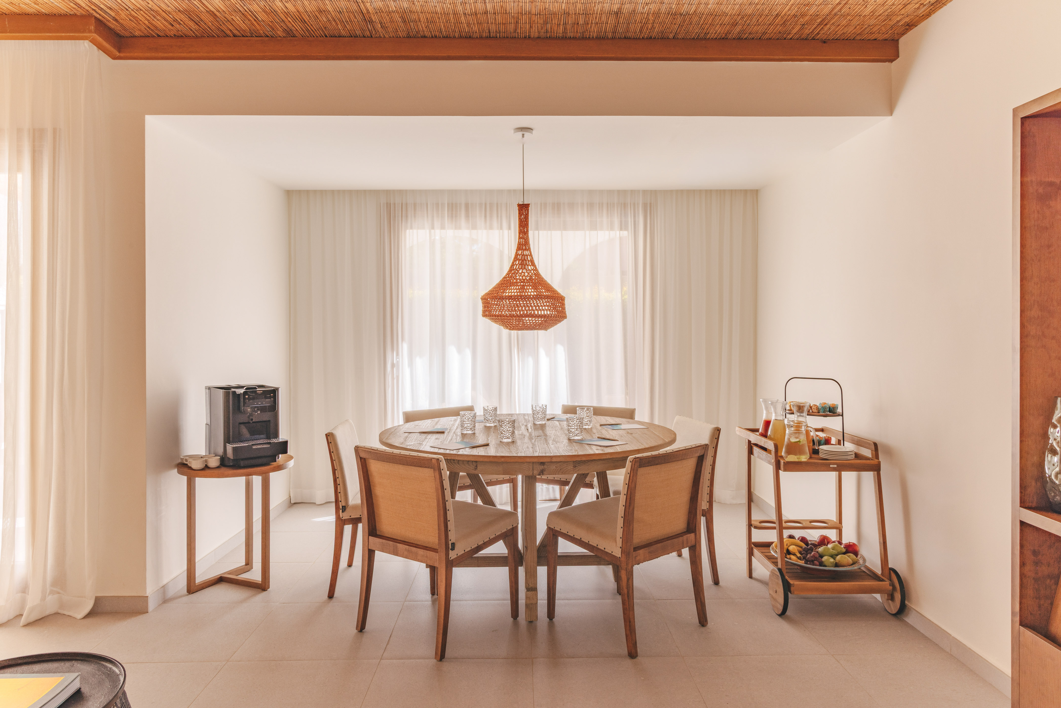 Dining area with wooden table, woven light, coffee, and breakfast cart.