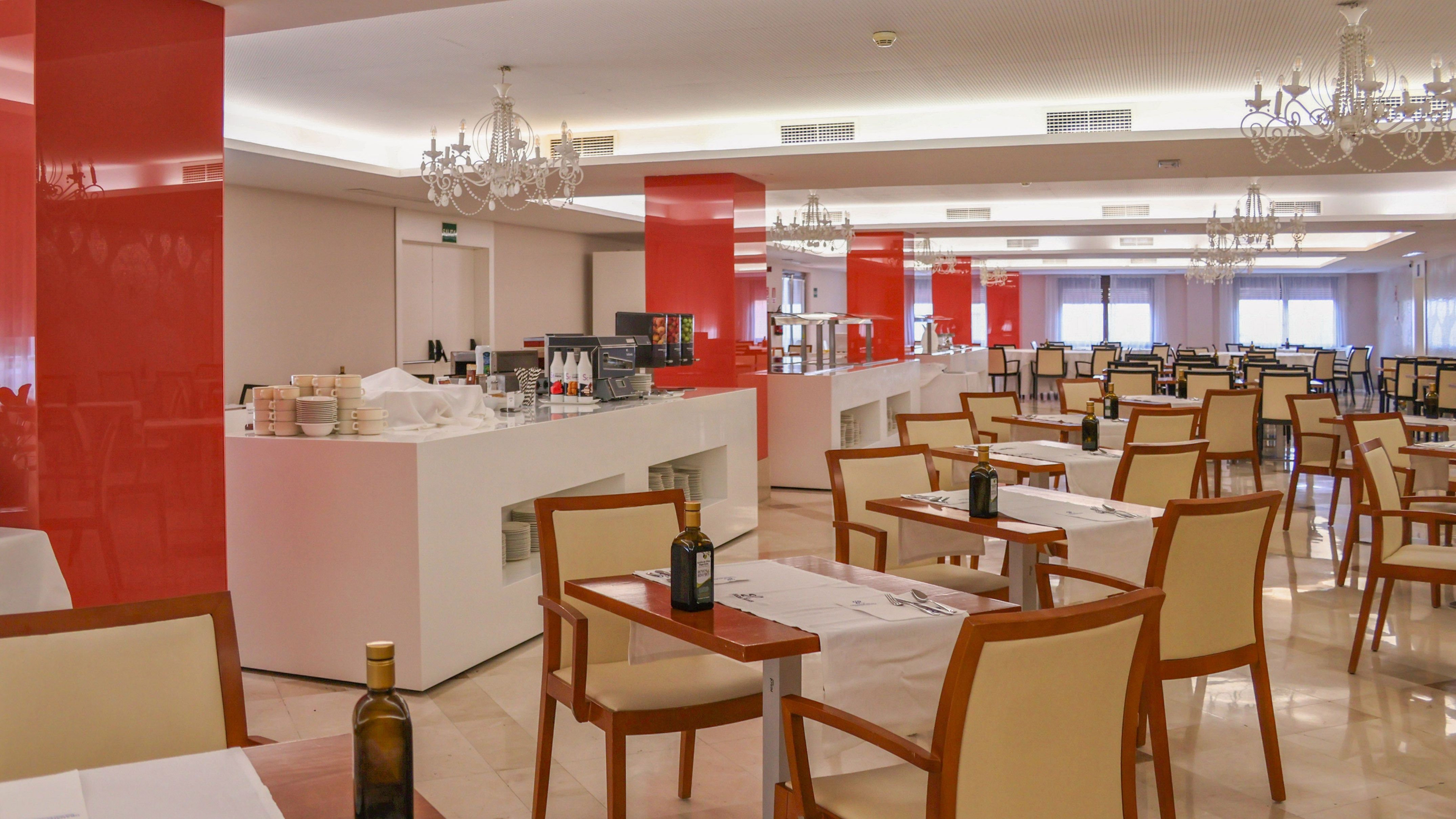 Spacious hotel buffet dining room with red pillars, white counters, and set tables.