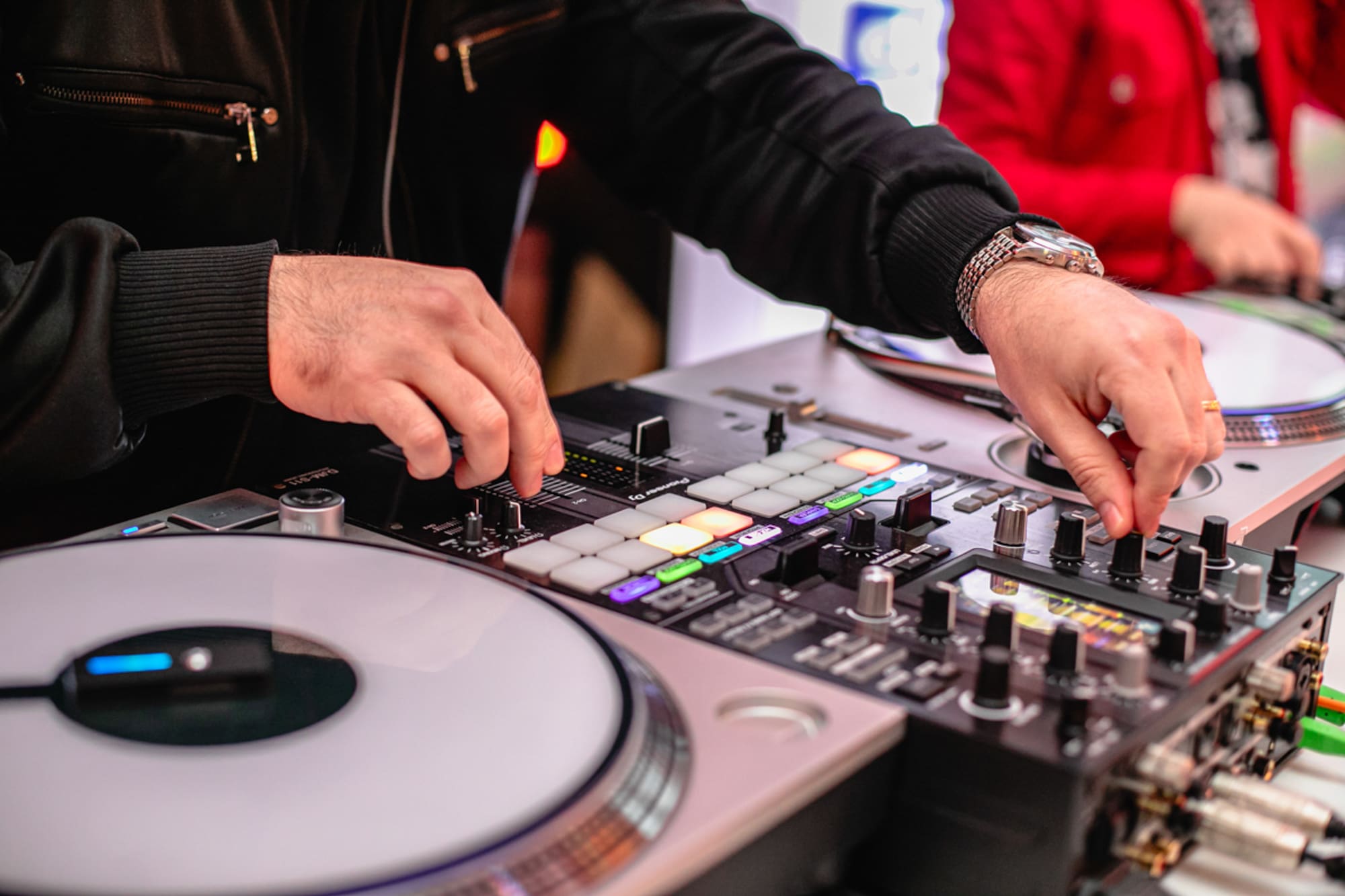 DJ's hands controlling a Pioneer DJ mixer with illuminated pads and turntable.