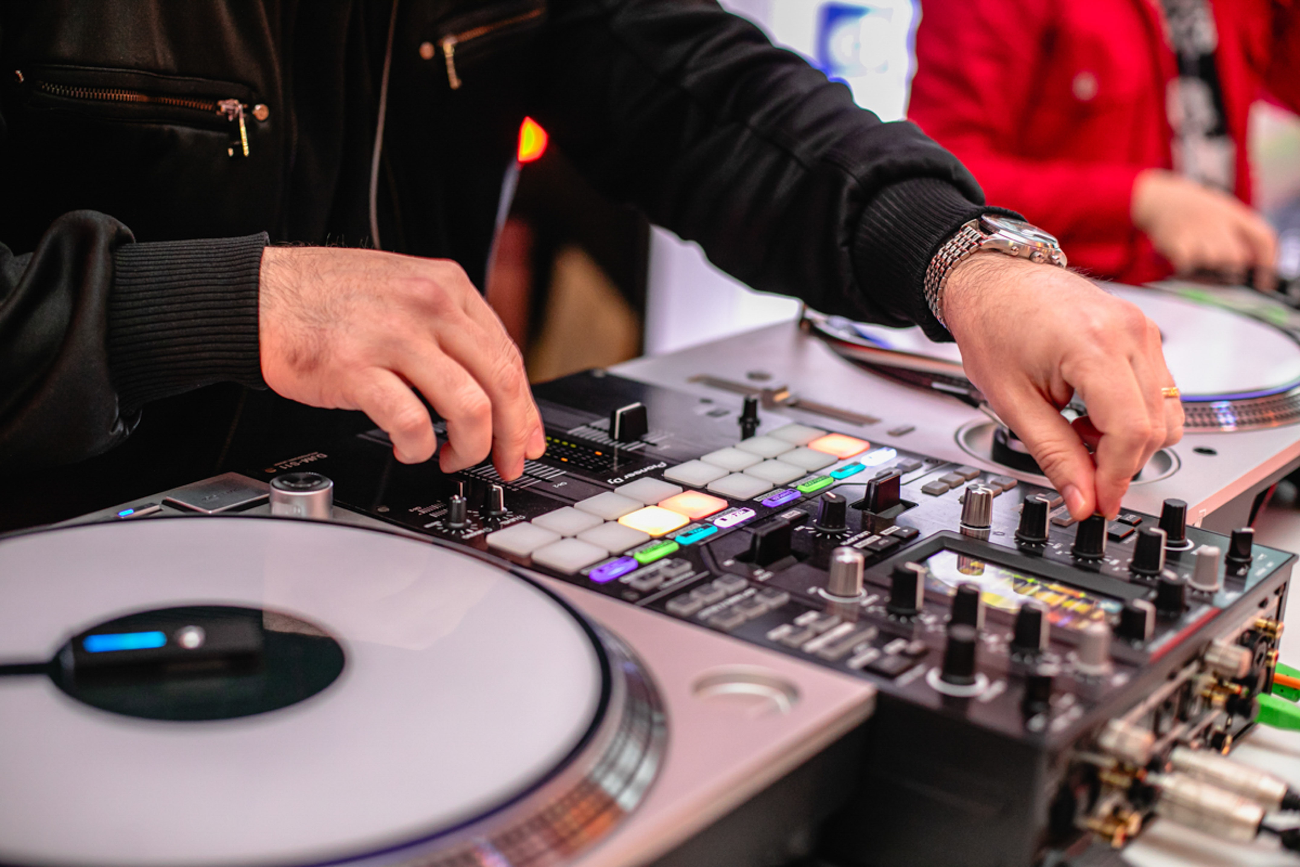 DJ's hands controlling a Pioneer DJ mixer with illuminated pads and turntable.