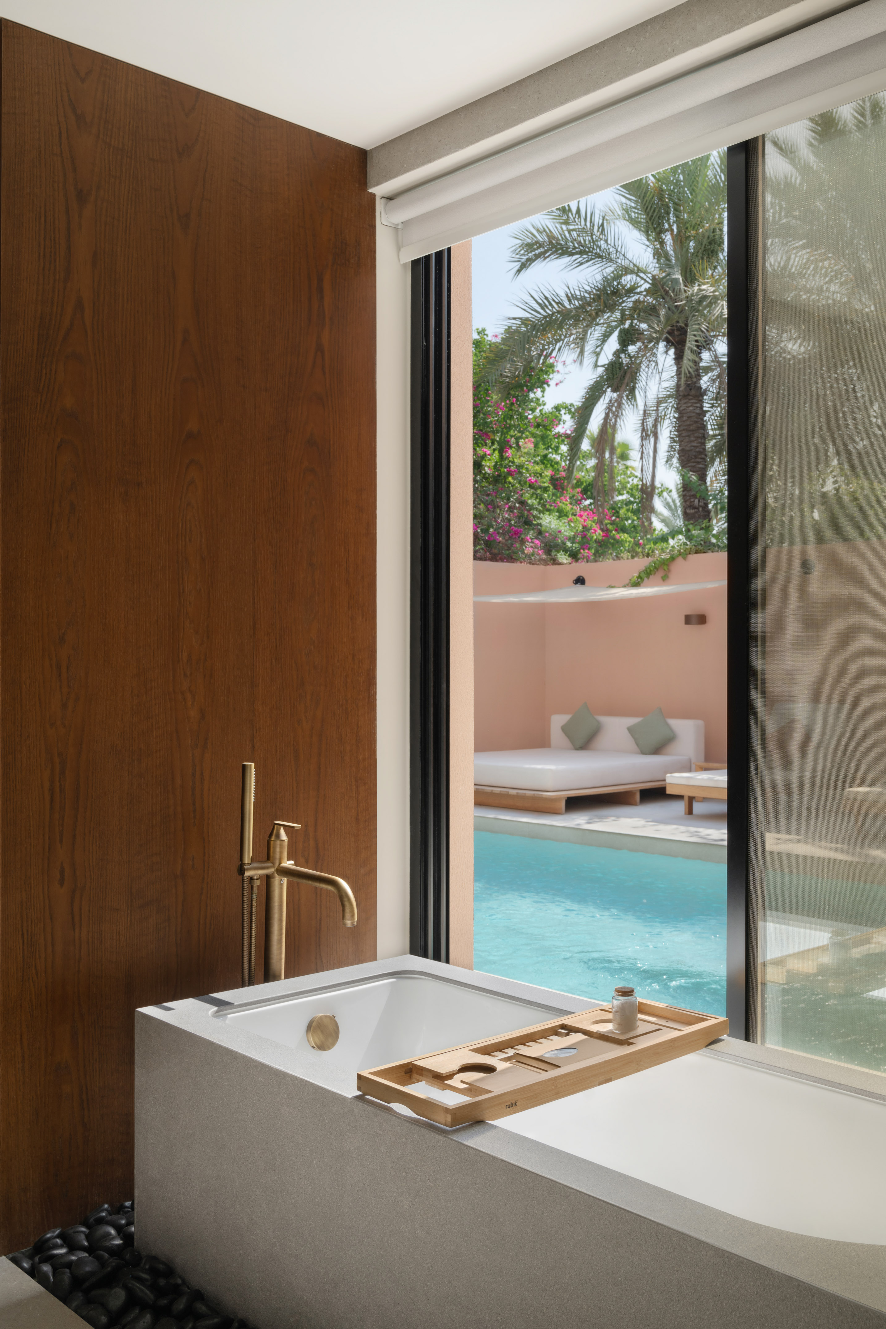 Modern bathroom with freestanding tub, brass faucet, and view of private pool.