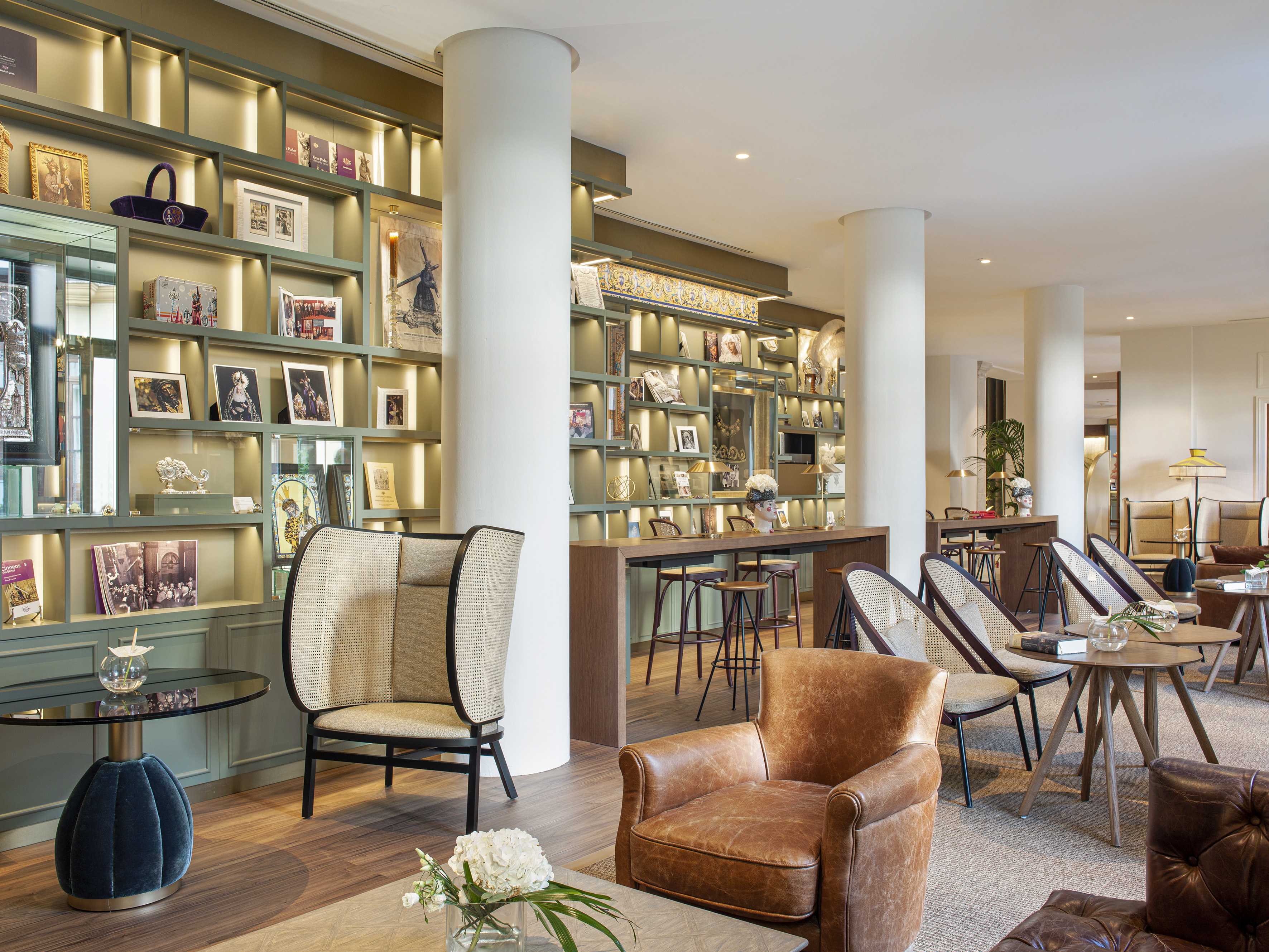Hotel lounge with green display shelves, leather armchairs, and rattan chairs.
