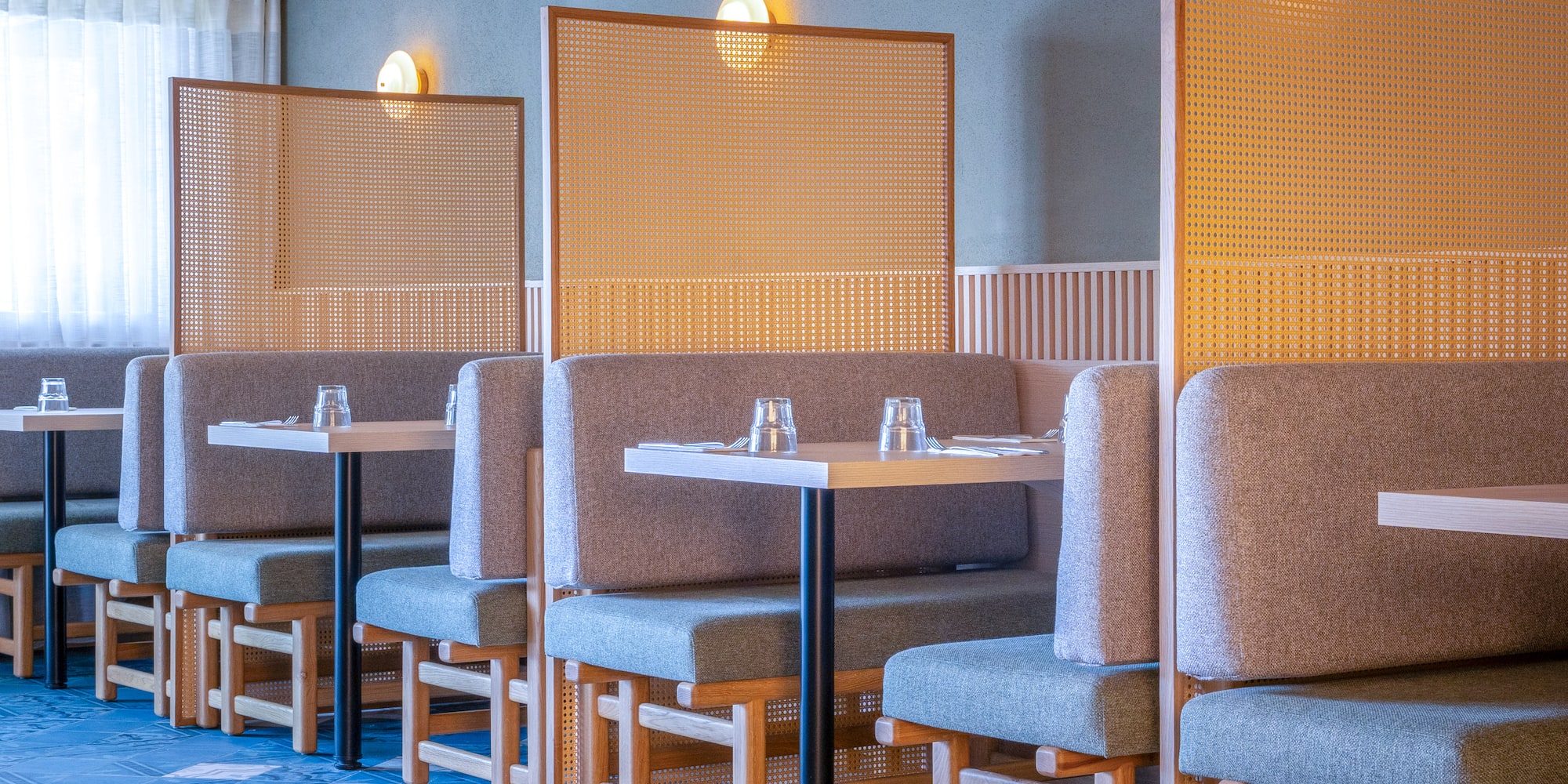 Modern restaurant interior with grey booths and cane privacy screens.